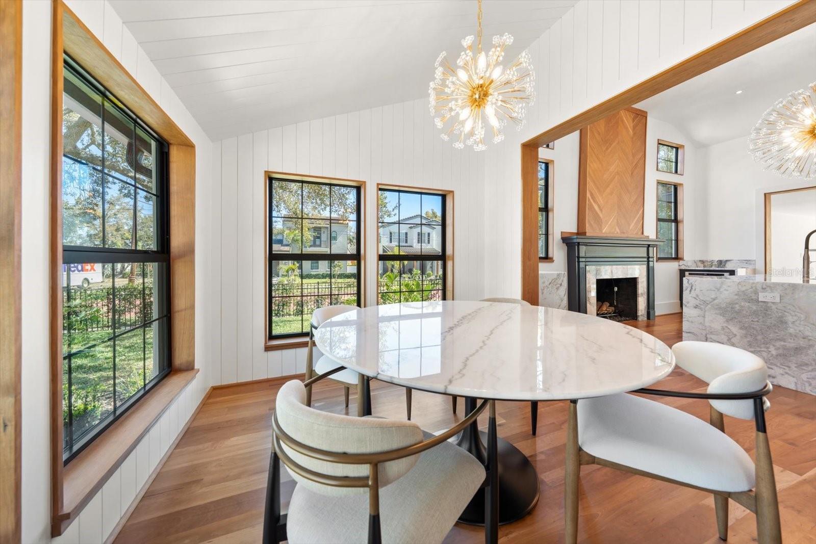 Dining room with shiplap walls and vaulted ceiling. Large windows and modern lighting mirroring lighting in the kitchen