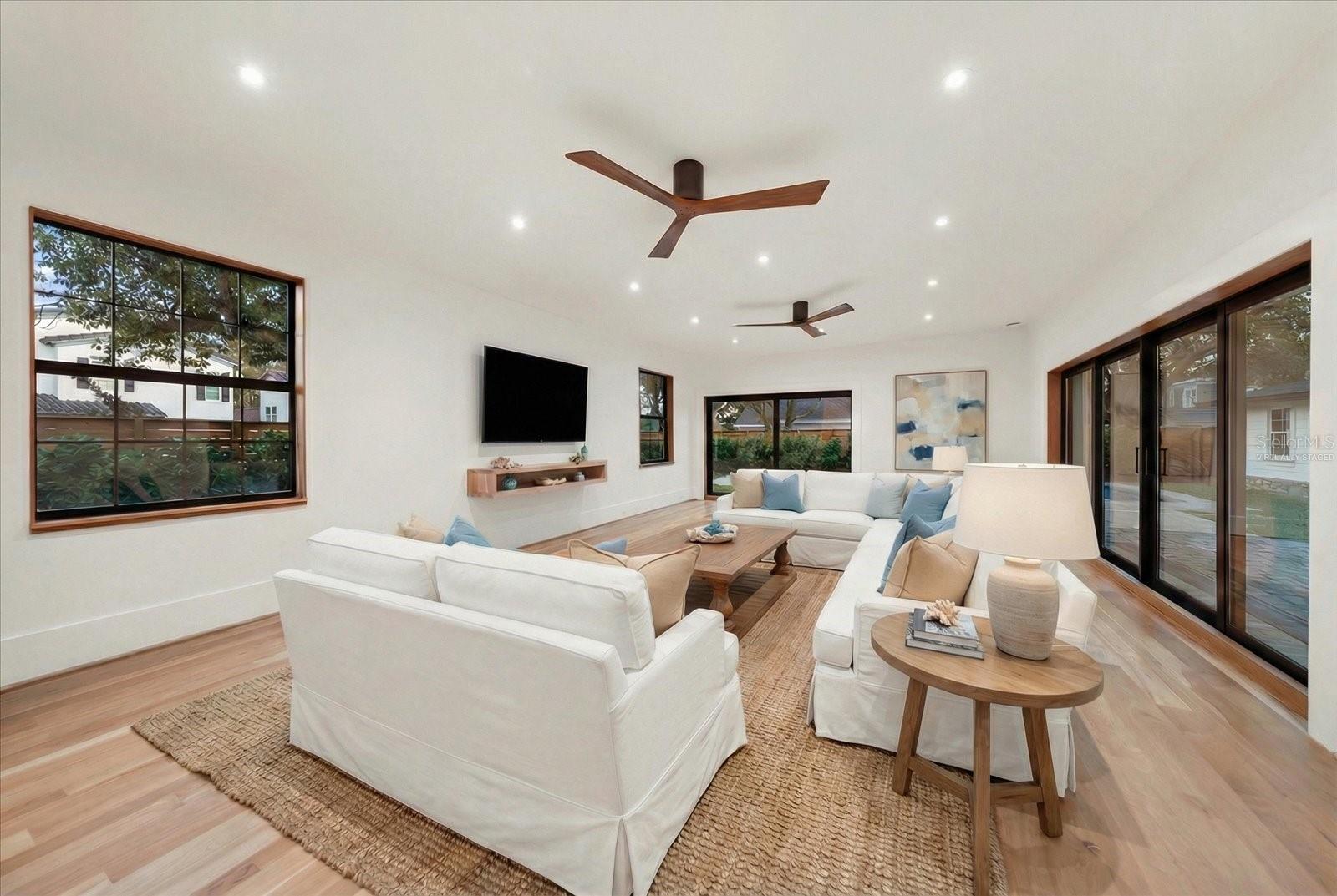 Spacious Great Room with floating shelves, many windows, and 2 sets of sliding glass to the pool to the brick paver entertainment space, and garage.  Virtually staged