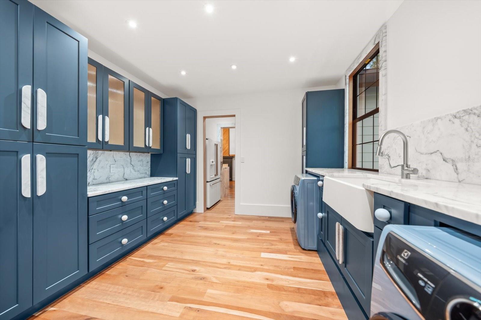 Scullery/laundry room with an abundance of solid wood cabinetry, apron front farmhouse sink, marble countertops, Electrolux washer & dryer.  Large windows overlooking backyard pool area
