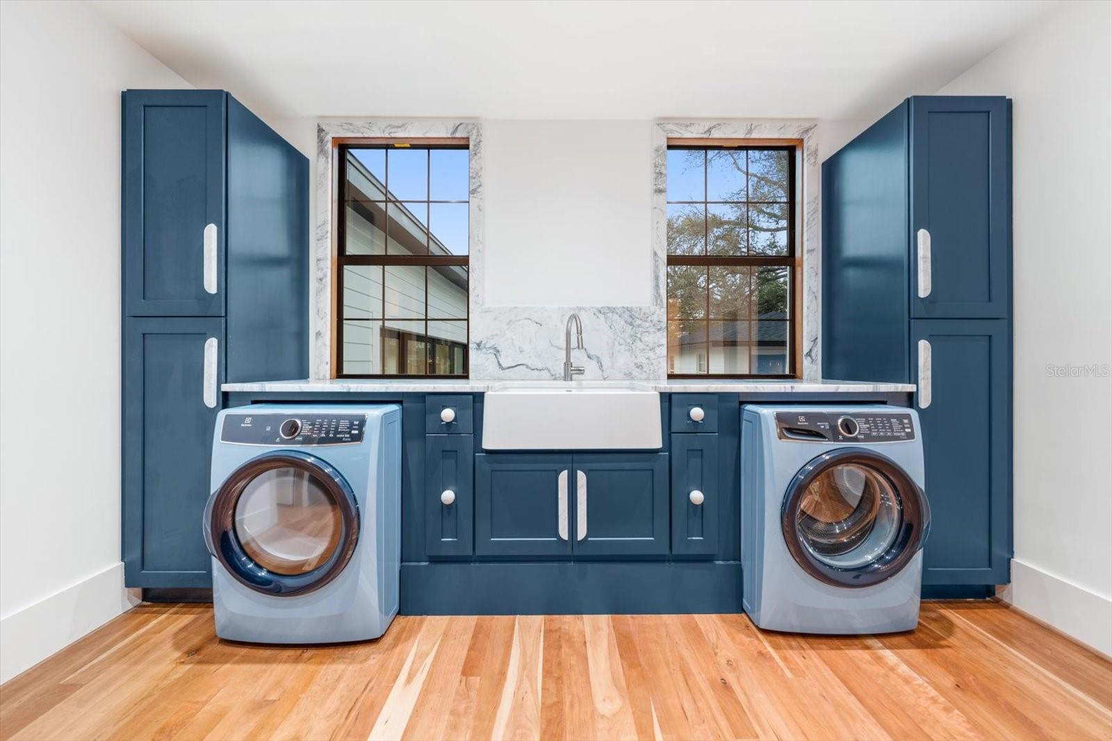 Scullery/laundry room with an abundance of solid wood cabinetry, apron front farmhouse sink, marble countertops, Electrolux washer & dryer.  Large windows overlooking backyard pool area