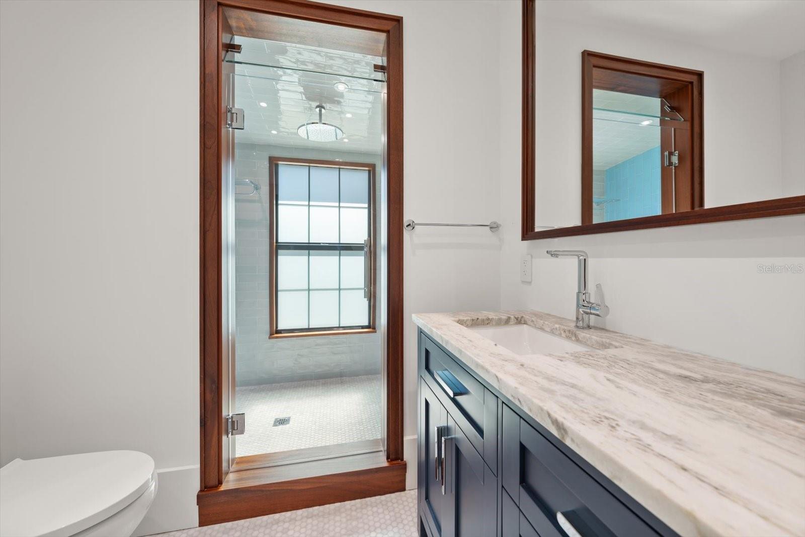 Stunning shower in hall bath, with mahogany framing around shower, window, and shower threshold and mirror. Bluetooth fan.