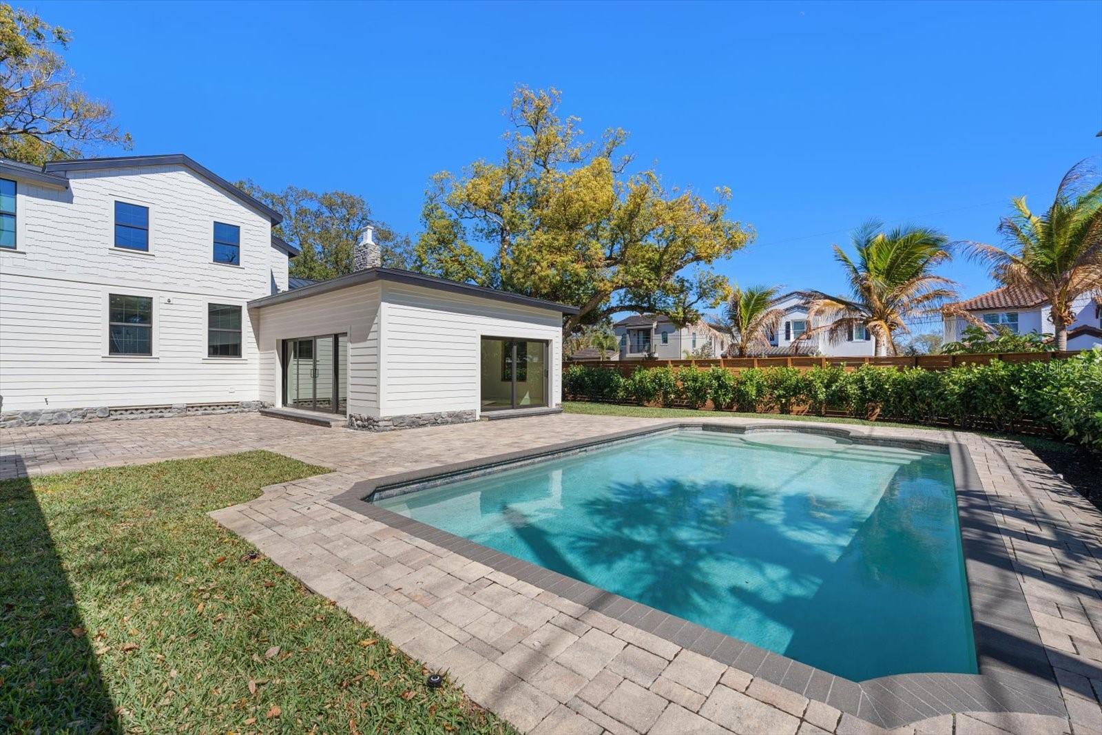 Expansive brick paver pool deck, outdoor living/entertaining space, surrounded by lush landscaping, lots of grass and beautiful 7' deep pool with sunshelf and lighting.