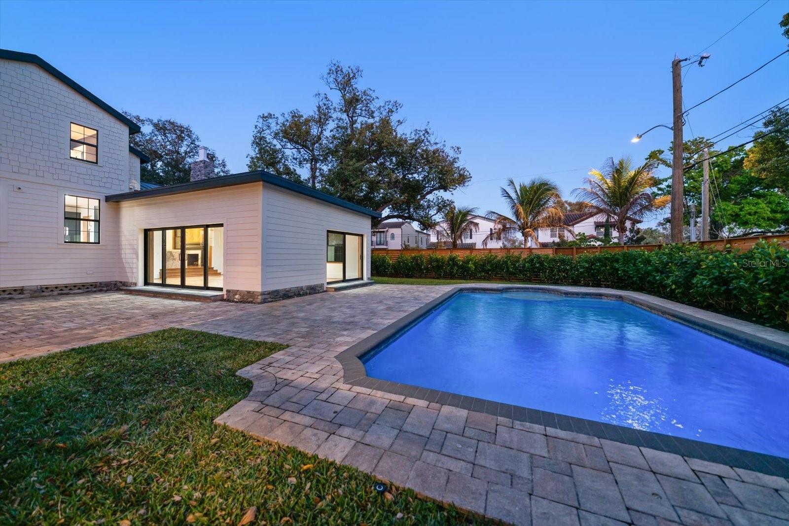 Great Room with 2 sets of sliding glass doors to the expansive brick paver pool deck, outdoor living/entertaining space, surrounded by lush landscaping, lots of grass and beautiful 7' deep pool with sunshelf and lighting.