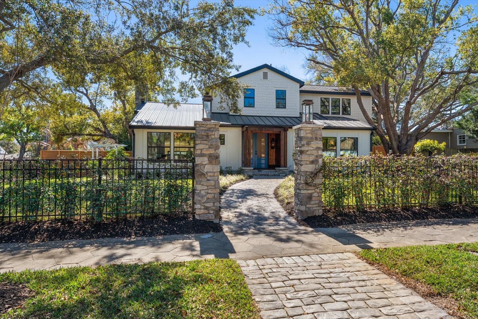 Front of home with wrought iron fencing with climbing Jasmine, beautiful stone walkway. Gas lanterns atop stone pillars at walkway entrance