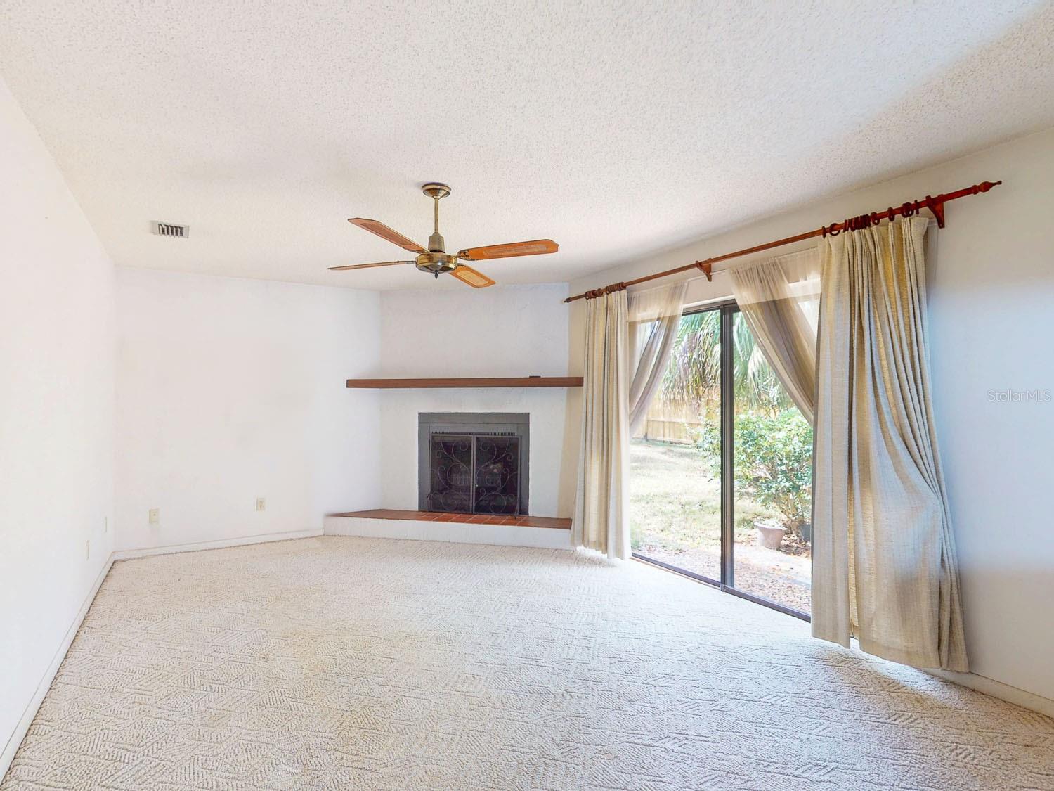 Bright family room area featuring a cozy fireplace, ceiling fan, and sliding door that opens to the backyard patio
