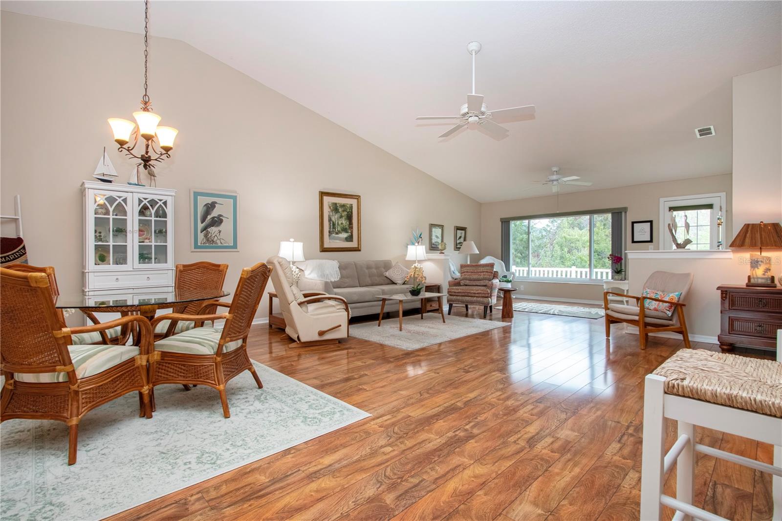 Living/dining area with view of Florida room and greenery.