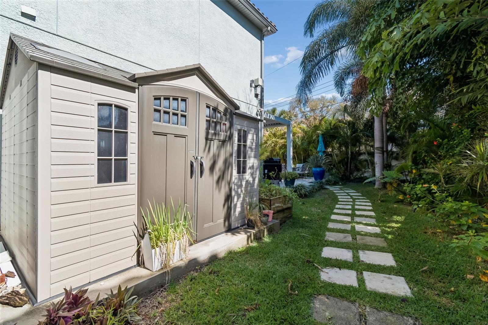 Garden pathway leads through lush landscaping to backyard storage shed.