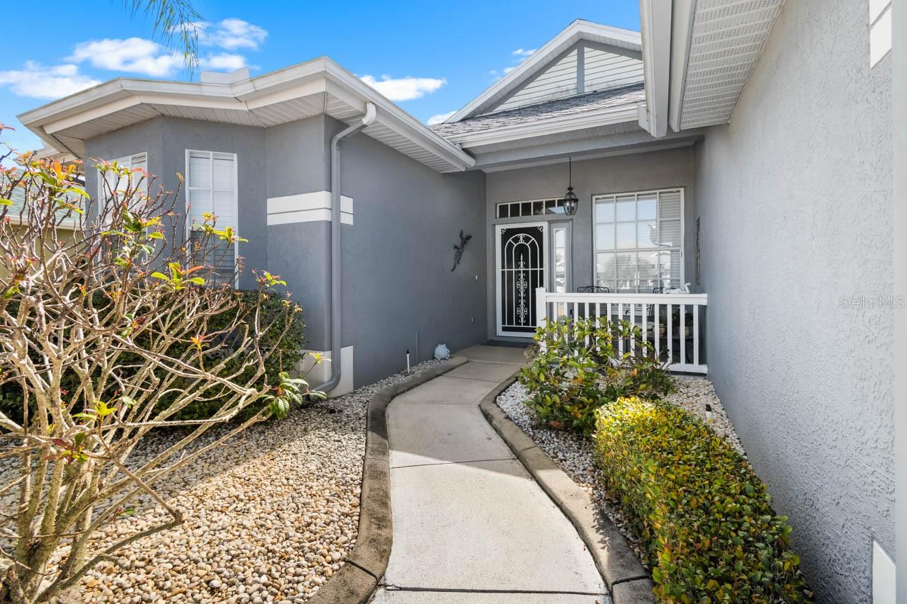 Welcoming front entrance featuring a charming winding walkway, meticulously maintained xeriscape landscaping for low-maintenance living, and a private gated courtyard entry.