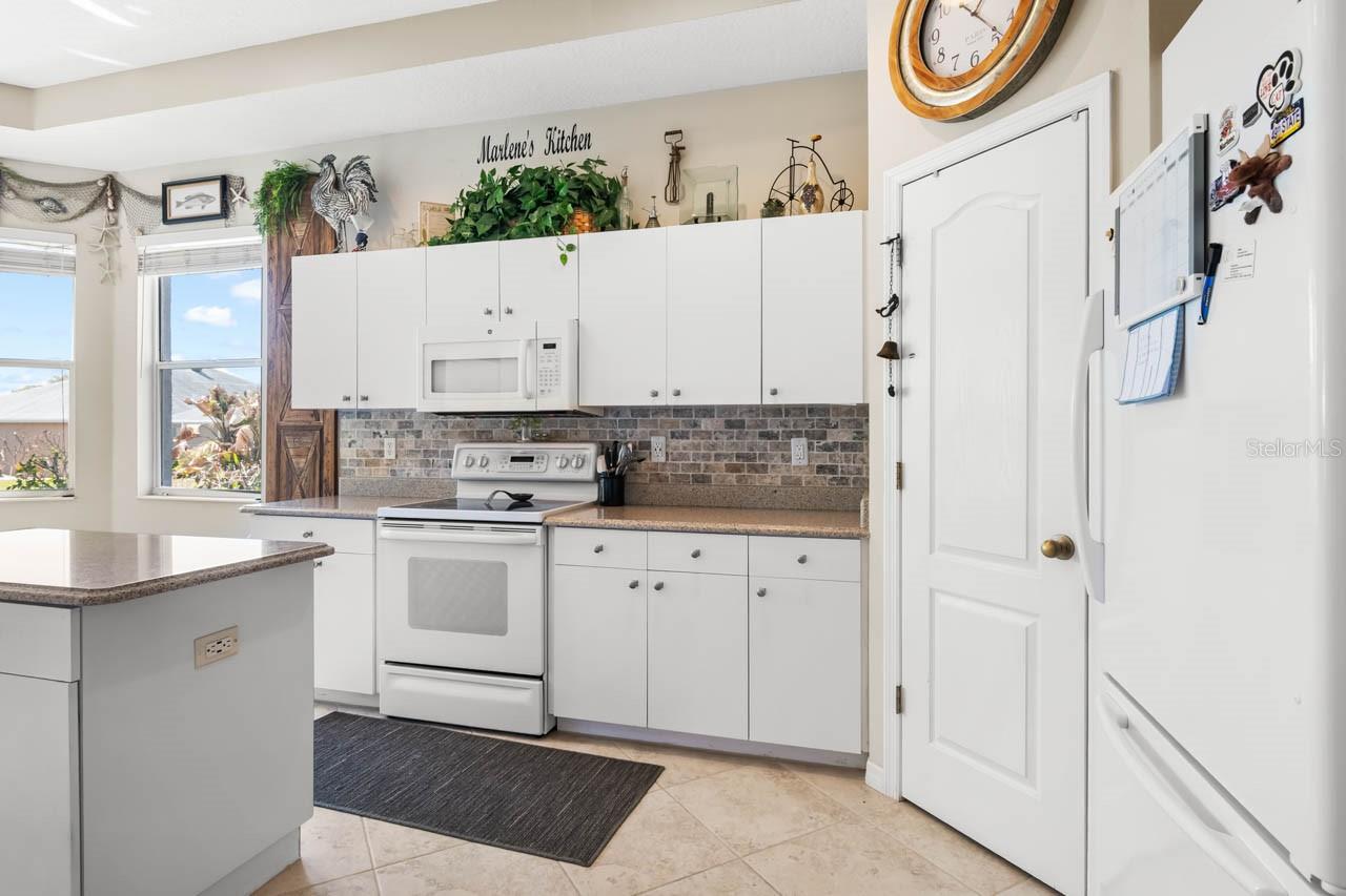 Modern and bright kitchen featuring crisp white cabinetry, a stylish tiled backsplash, and durable stone-look countertops. The open layout includes a convenient center island, recessed lighting, and a breakfast nook area, making it as functional as it is beautiful for everyday cooking and entertaining.