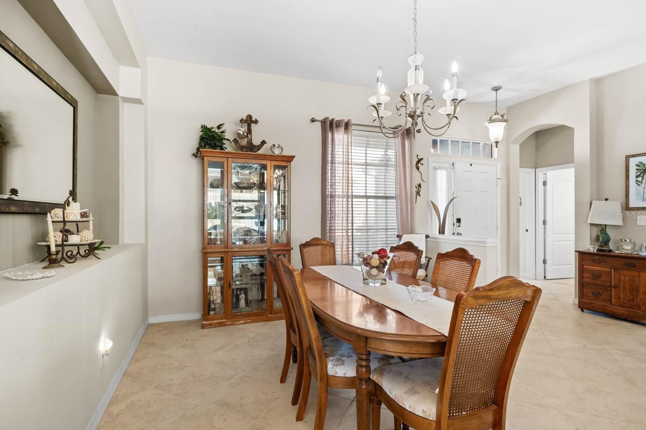 Elegant formal dining room featuring a classic chandelier, neutral tile flooring, and an architectural tray ceiling. The open layout provides a direct view into the welcoming foyer, making this the perfect space for hosting dinner parties or holiday gatherings