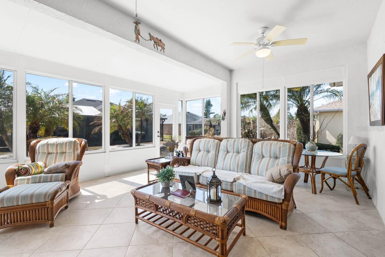 Expansive and light-filled Florida room featuring wall-to-wall windows that showcase peaceful backyard views. This versatile bonus living space includes neutral tile flooring, a cooling ceiling fan, and plenty of room for both lounging and dining, making it the perfect year-round retreat.