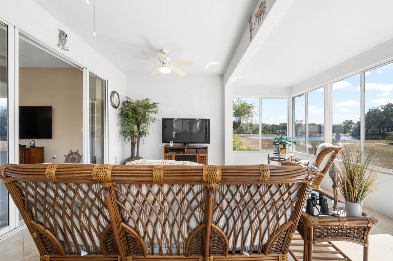 Serene and expansive Florida room offering picturesque water views and a peaceful retreat for relaxation. This bright, airy space features wall-to-wall windows that invite the outdoors in, complemented by cool neutral tile flooring and a ceiling fan for year-round comfort.