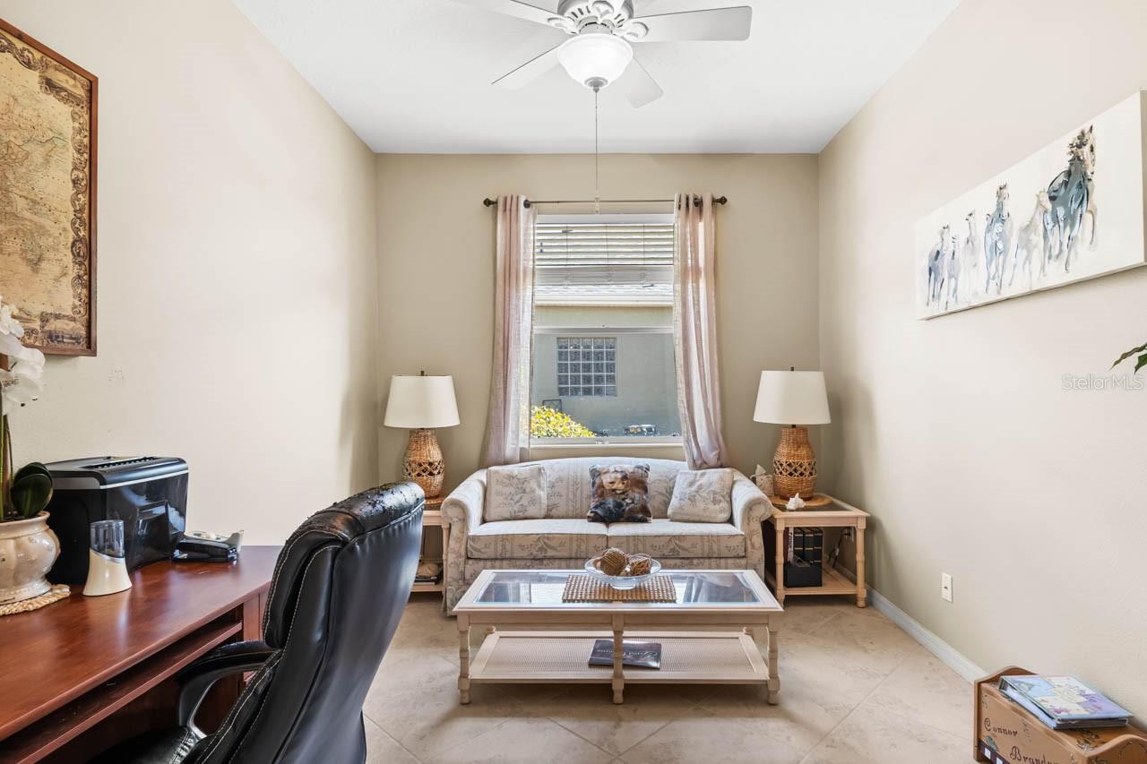 Versatile den featuring bright, neutral tones, high ceilings with a cooling ceiling fan, and large-format tile flooring. This flexible space is perfect for a home office, hobby room, or a quiet reading retreat.