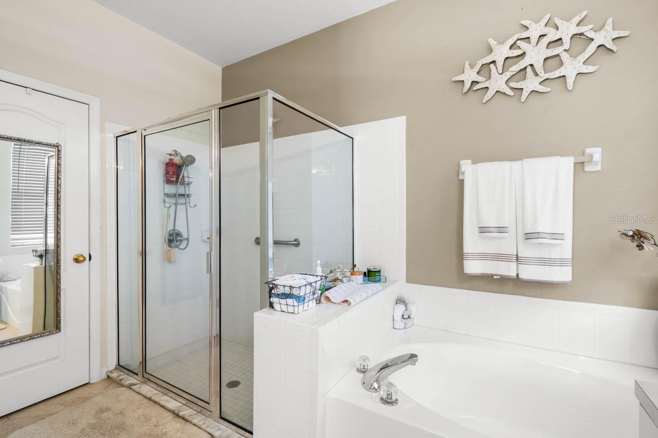 "Luxurious Primary Bathroom featuring a spa-inspired soaking tub and a separate glass-enclosed walk-in shower. The neutral tile work, bright white cabinetry, and serene coastal decor create a relaxing, retreat-like atmosphere.