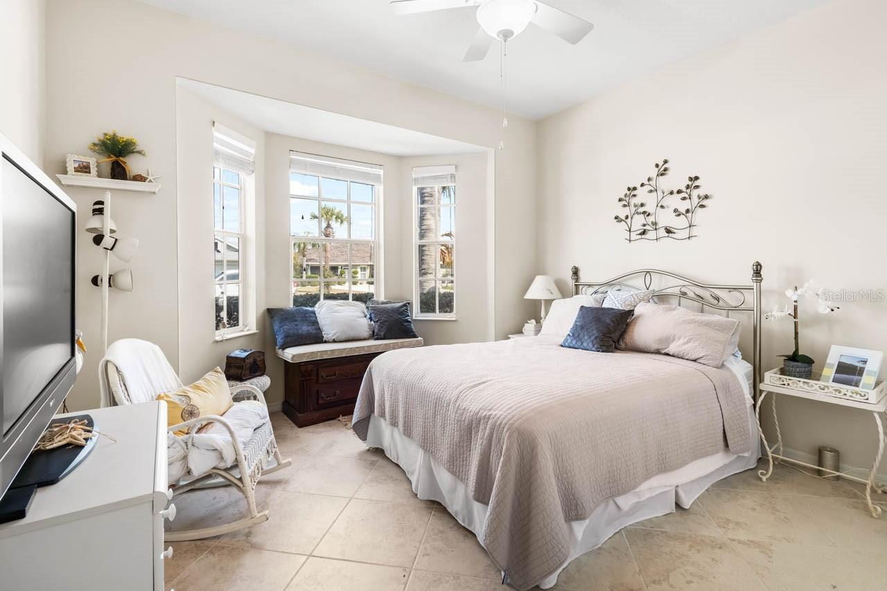 "Bright and inviting second bedroom featuring a charming bay window with a built-in bench seat, perfect for a sunny reading nook. This spacious room includes neutral tile flooring, a cooling ceiling fan, and ample space for guests to feel right at home.