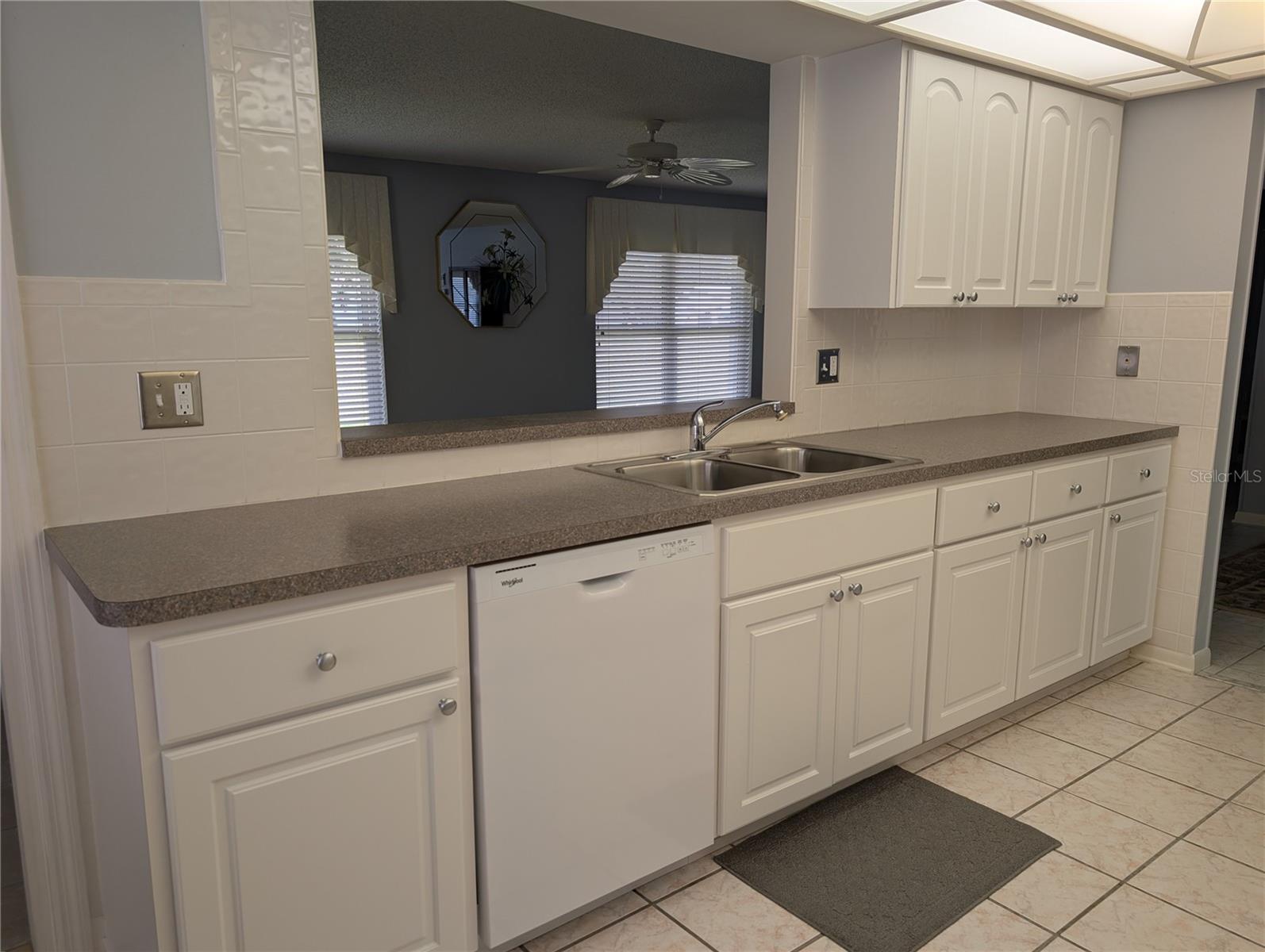Immaculate kitchen features updated white cabinetry, tile backsplash, laminate countertops, stainless steel double sink and new white Whirlpool dishwasher (2025). Insinkerator garbage disposal (2023) installed under sink.