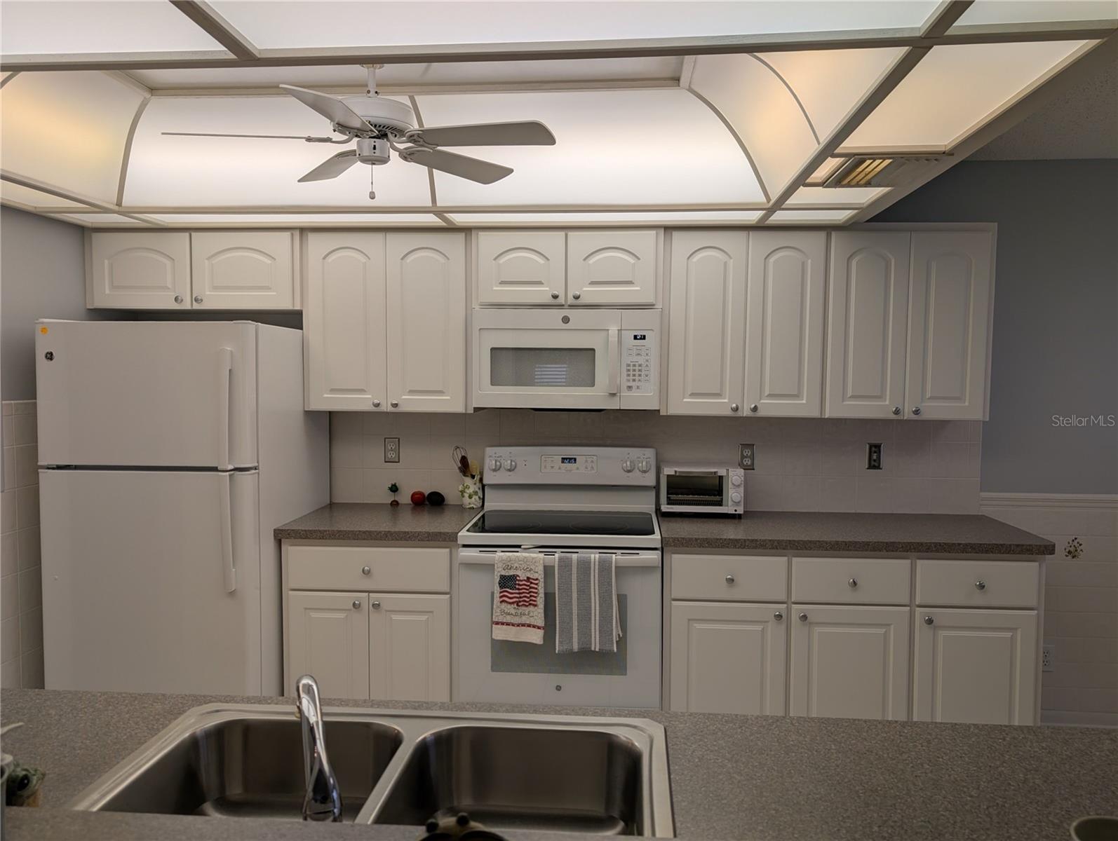 White GE appliances include top freezer refrigerator (2019), glass cooktop range/oven (2019) and microwave hood (2025).