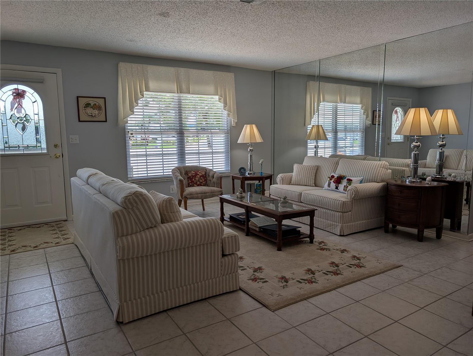 View of front entry from living room.  Welcoming decor features soft colors, ceramic tile flooring, Venetian blinds with fabric valance (2010)...turnkey condition.