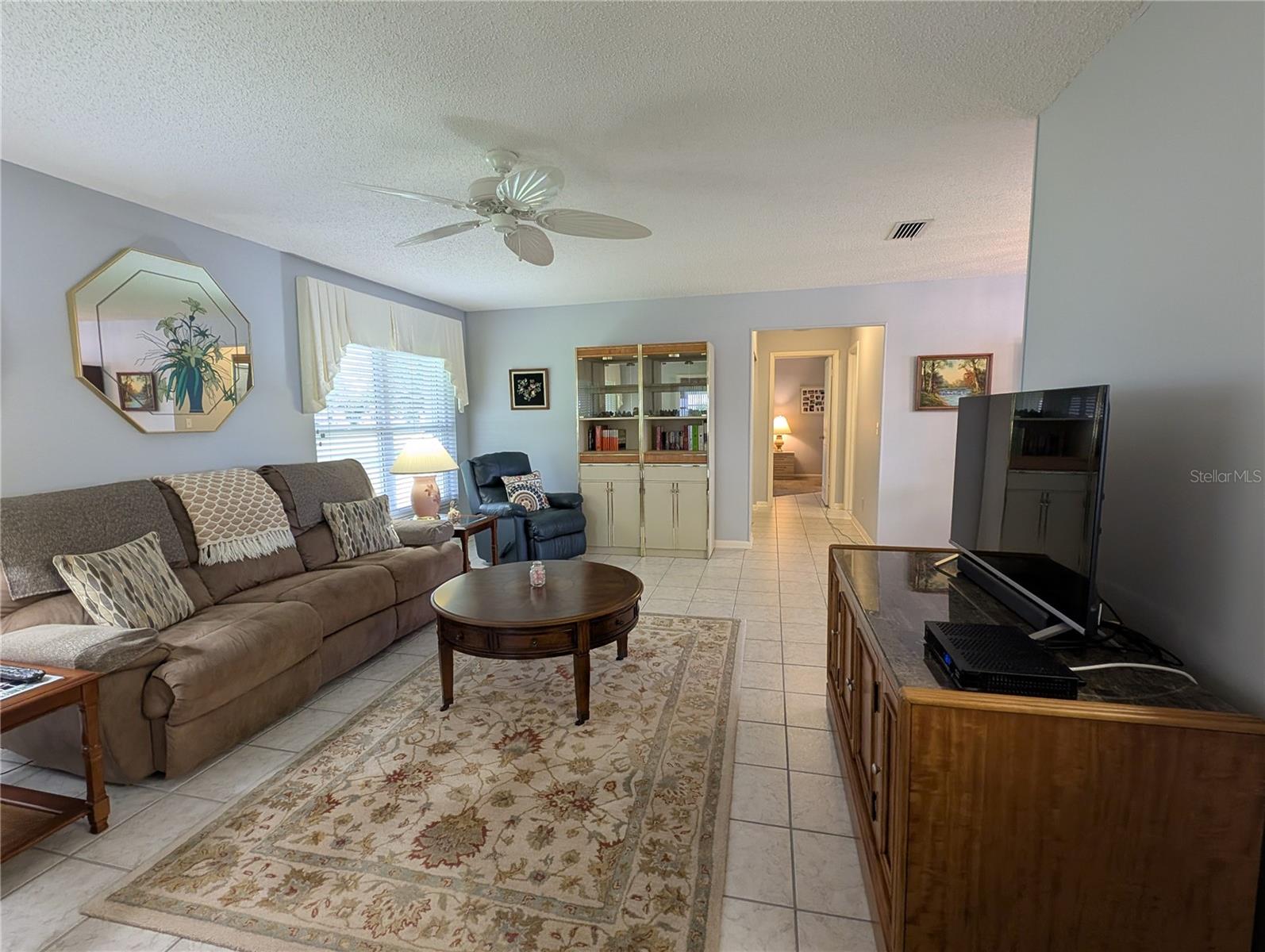 View from Bonus room thru Florida down hallway leading to Primary bedroom.   Spacious Florida room features ceramic tile flooring, soothing decor, Venetian blinds w/valances and updated ceiling fan. Dining room is to right of hallway entrance.  The huge windows not only provide natural light and ventilation but offer an outstanding parklike view of spacious backyard.