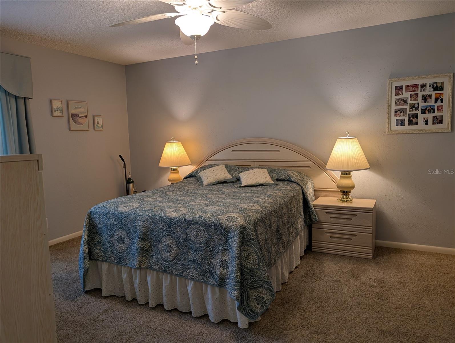 View of primary bedroom from hallway entry. Spacious primary bedroom features neutral carpeting, updated ceiling fan and soothing decor.