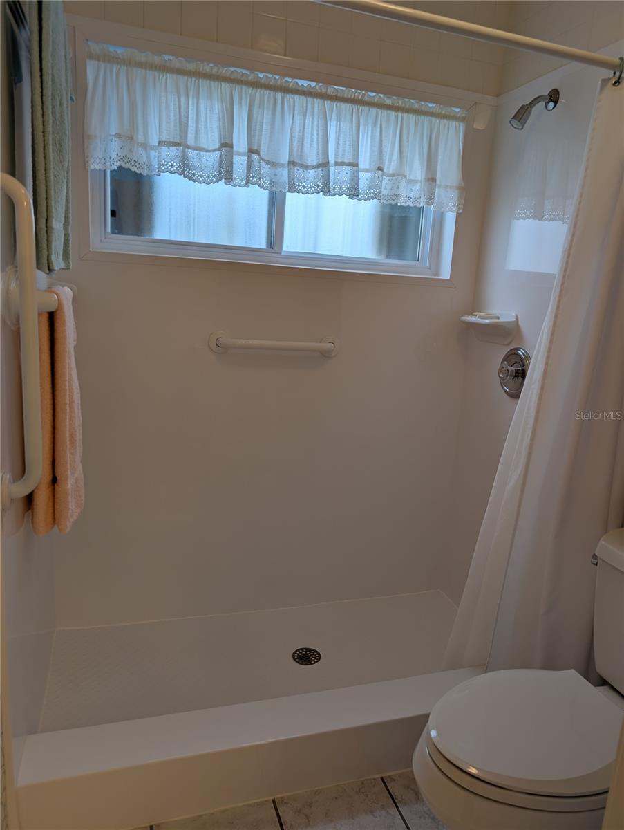 Close up view of renovated shower featuring grab bars for safe access, window for extra light/ventilation and low maintenance shower surround.