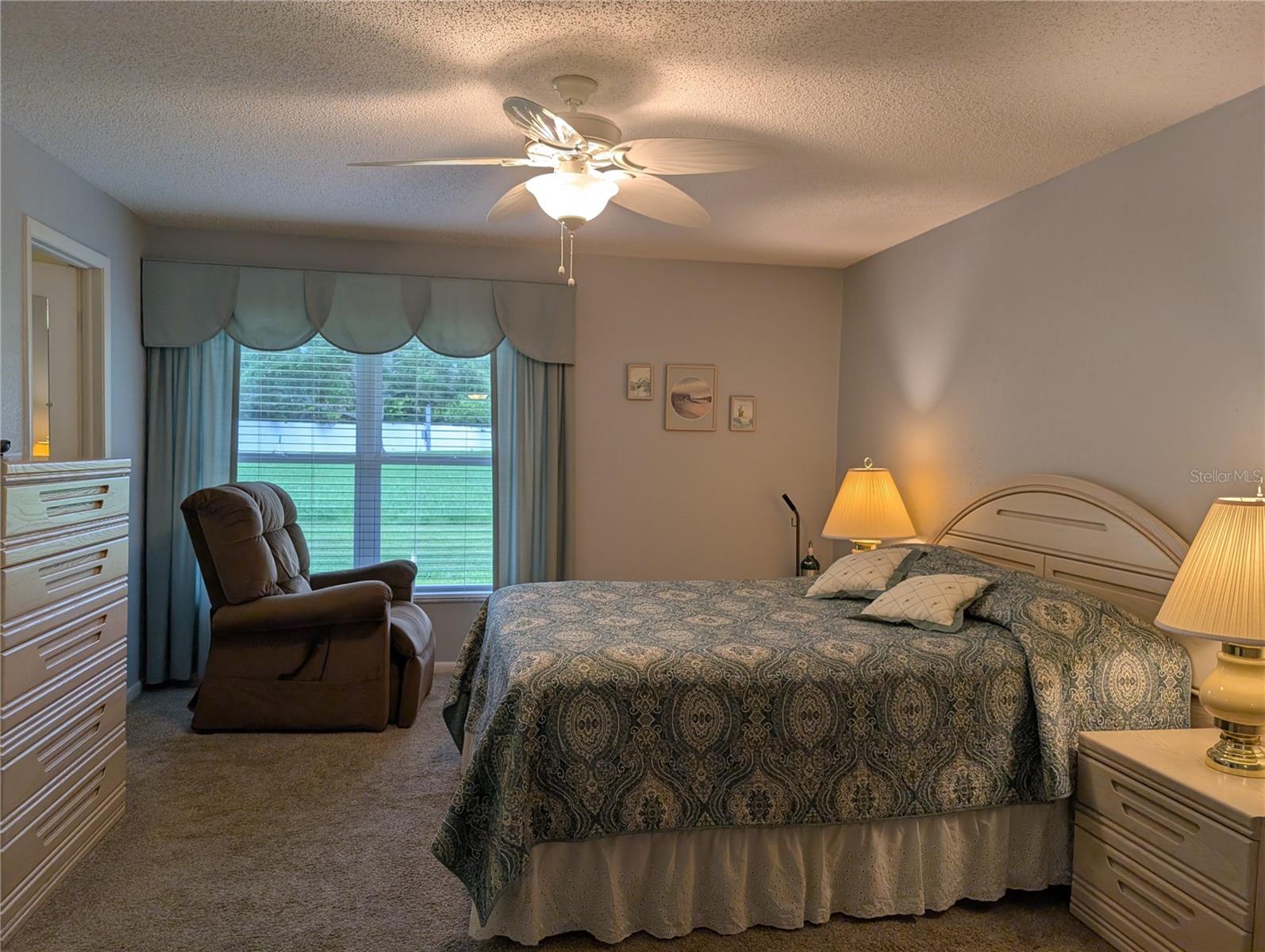 View thru primary bedroom from bathroom.  Spacious walk-in closet on left, custom window treatment w/Venetian blinds and another awesome backyard view.