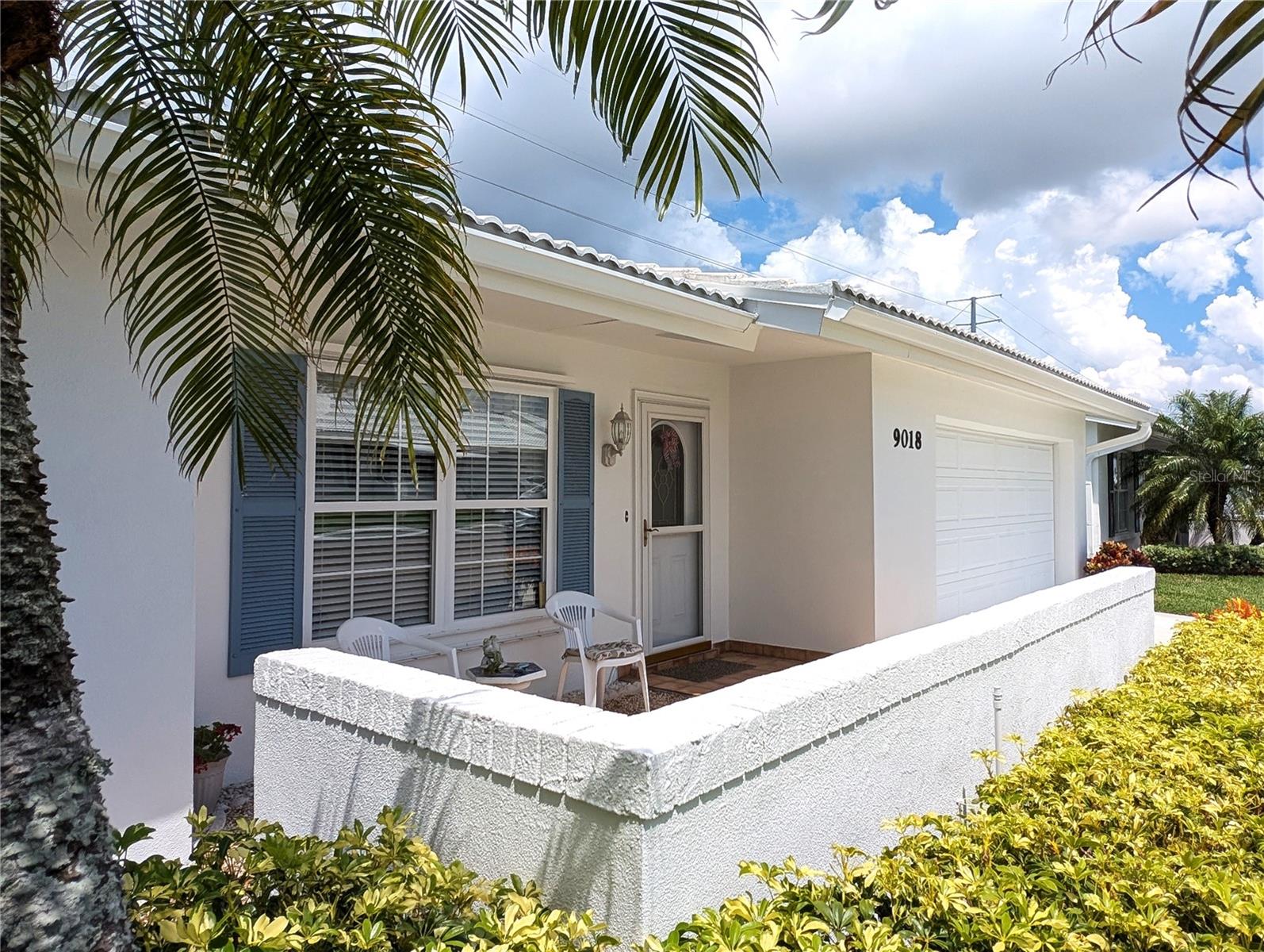 Exterior view of front porch main entry.  Exterior features included double pane windows w/storm protection by accordion shutters (2008) or NuVue storm panels, gutters/downspouts (2006) and new white tile roof (2023).  Tile roof included addition of 3rd nail in trusses and installation of Ridge Vent Rain Diverters (2025).