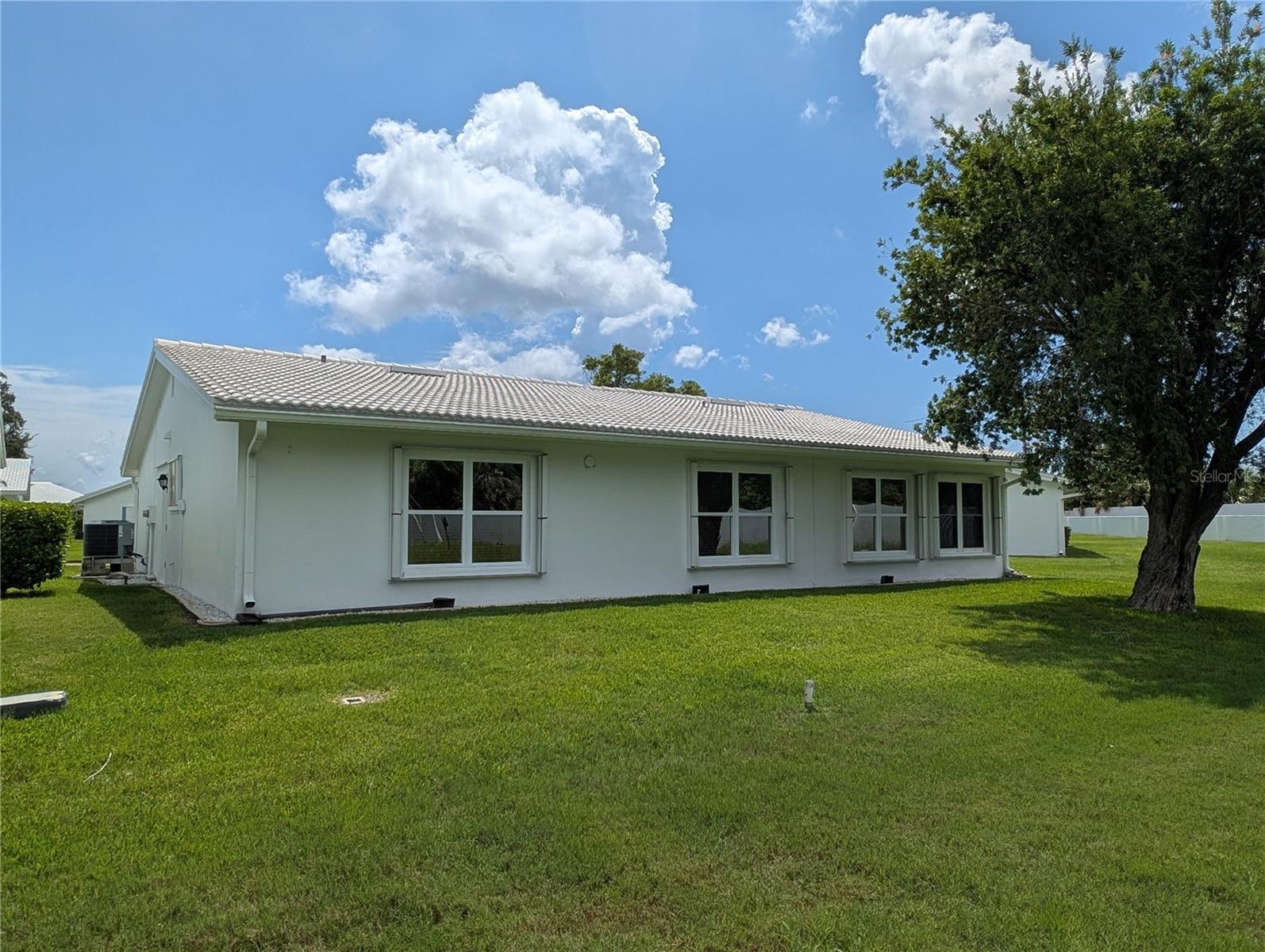 View of rear exterior.  Features include white tile roof w/ridge vent rain diverters, double pane windows w/accordion storm shutter protection and gutters/downspouts. Clothesline setup allowed in backyard.