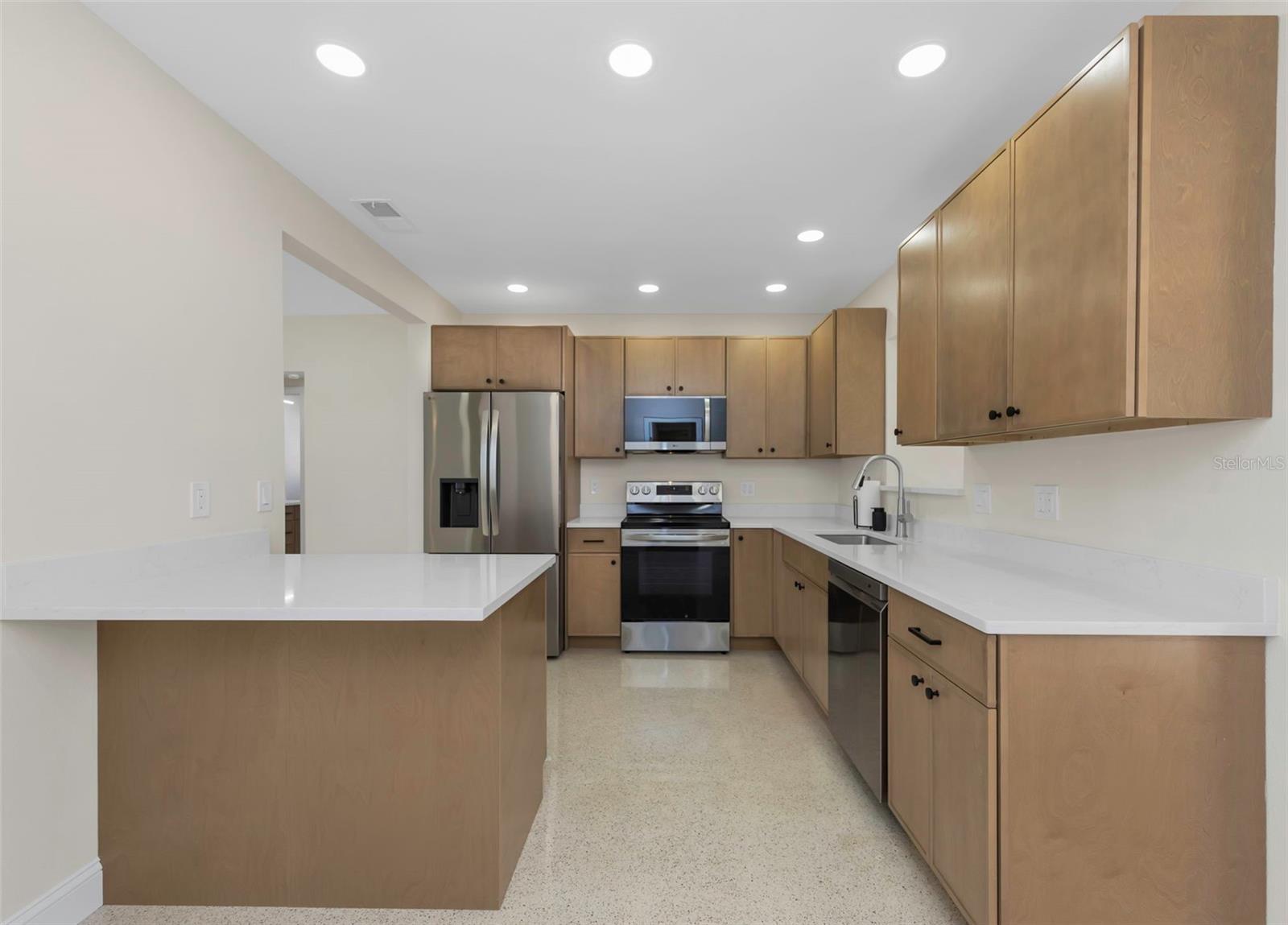 Kitchen includes custom, soft-close wood cabinetry, elegant quartz countertops, and recessed lighting.