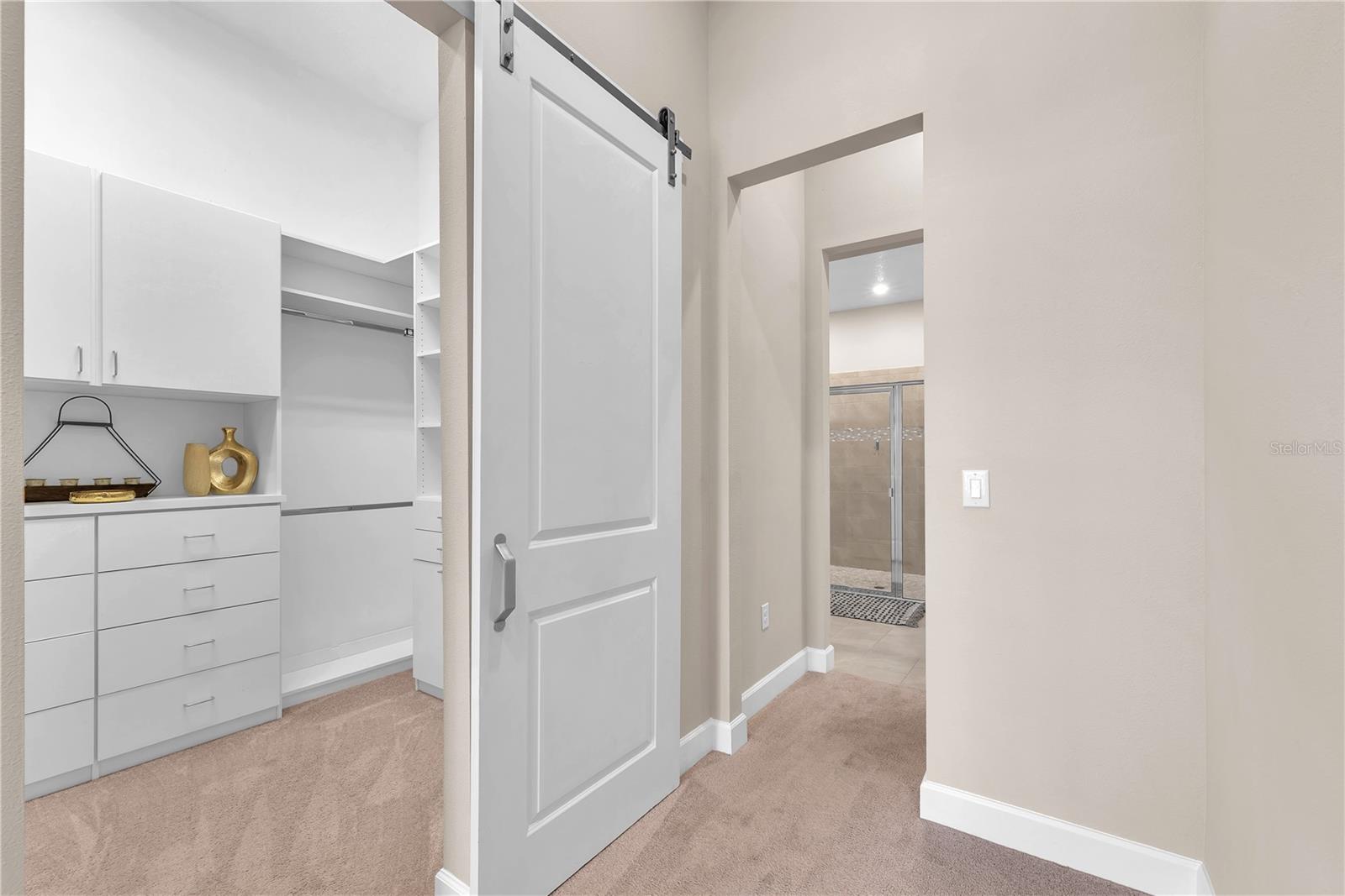 An enormous walk-in closet with built-in drawers and cabinets is tucked behind a sliding barn door.