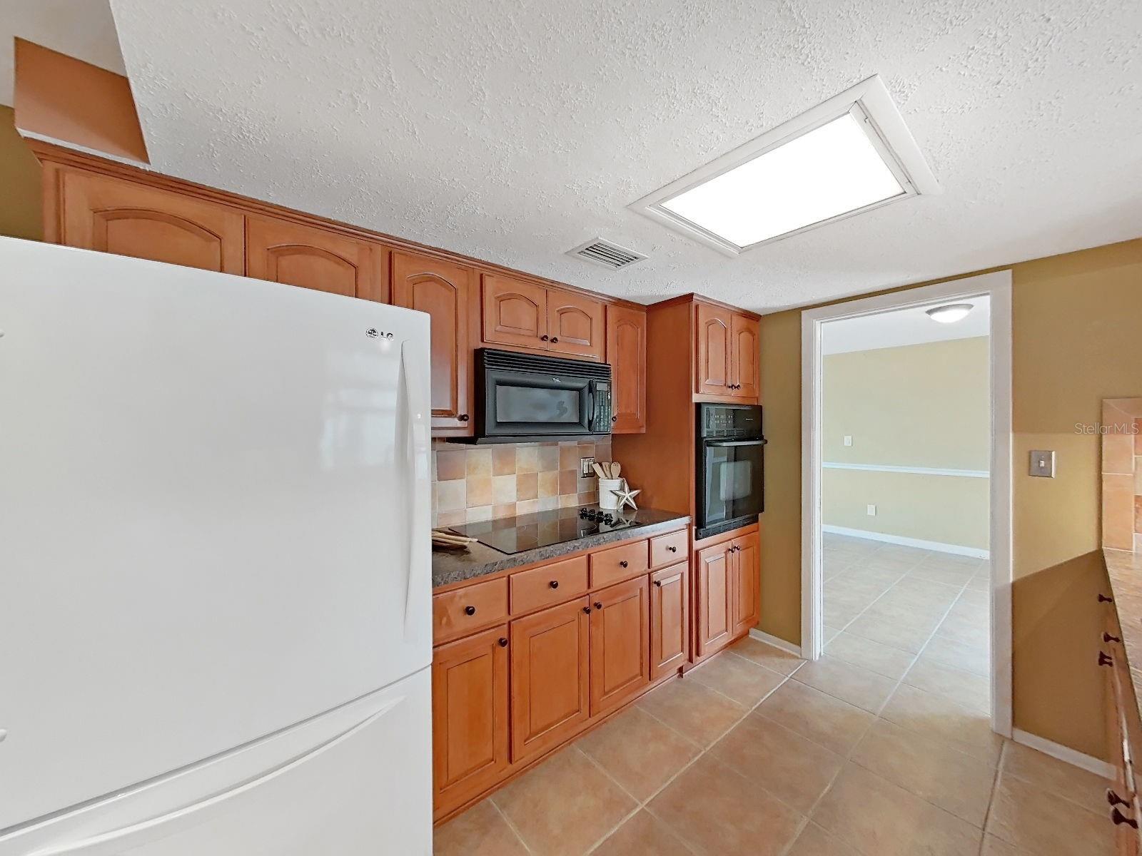 Kitchen with built-in microwave, wall oven, and neutral tile backsplash & flooring.