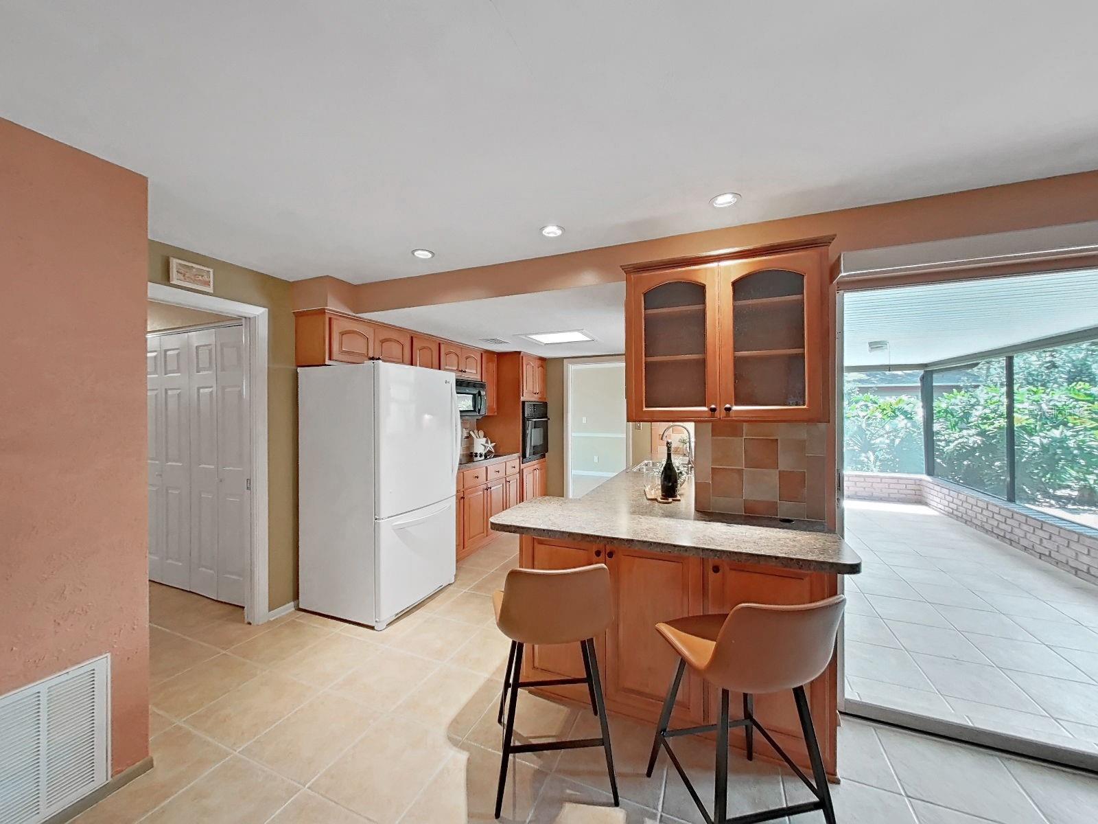 Functional Kitchen peninsula with bar seating- perfect for casual dining or a glass of wine! Complemented by glass-front cabinetry, lower cabinet storage, overhead accent lighting, & glass door overlooking the screened lanai.