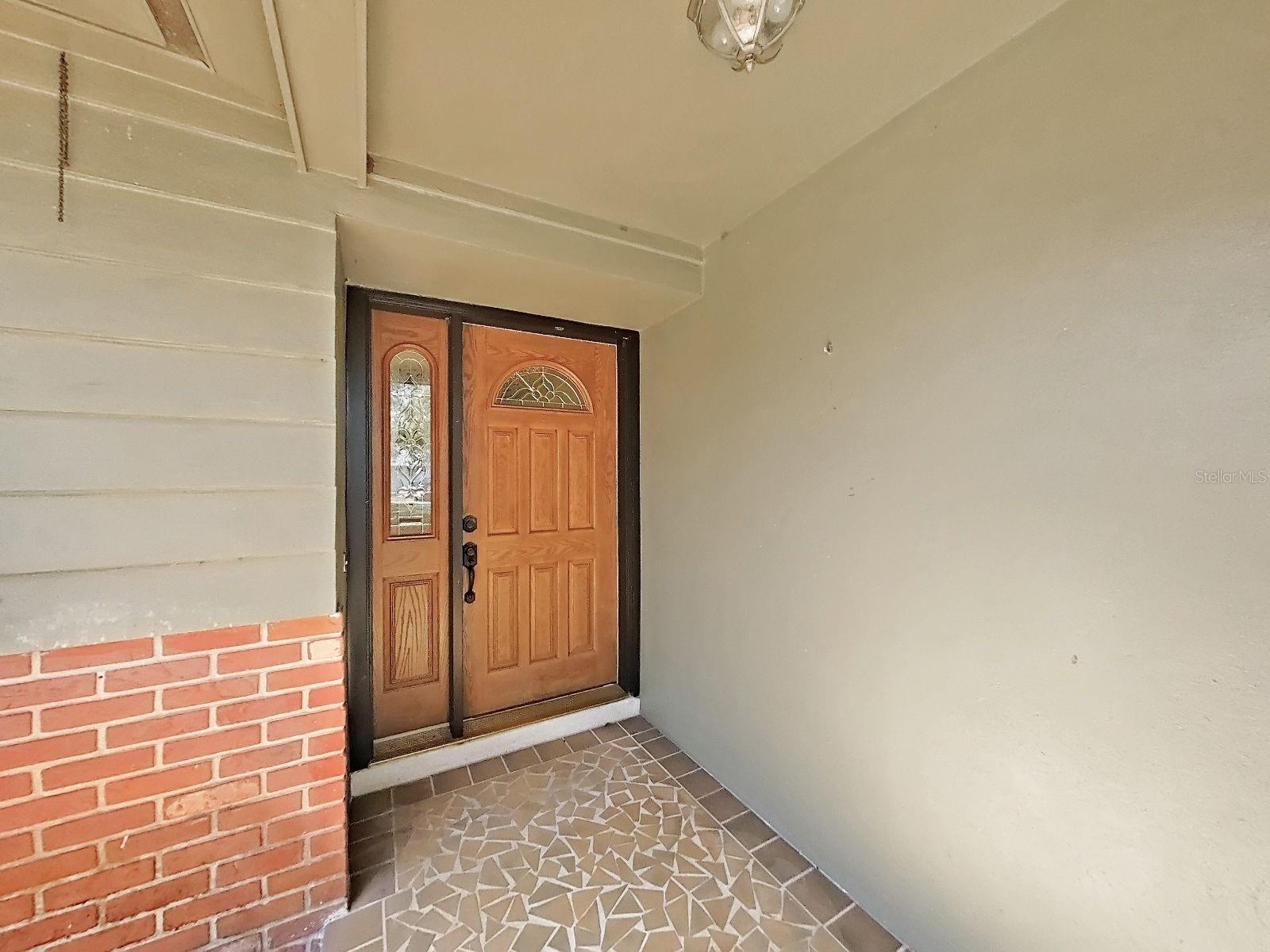 Charming front porch features a classic door with decorative glass and unique mosaic tile flooring.
