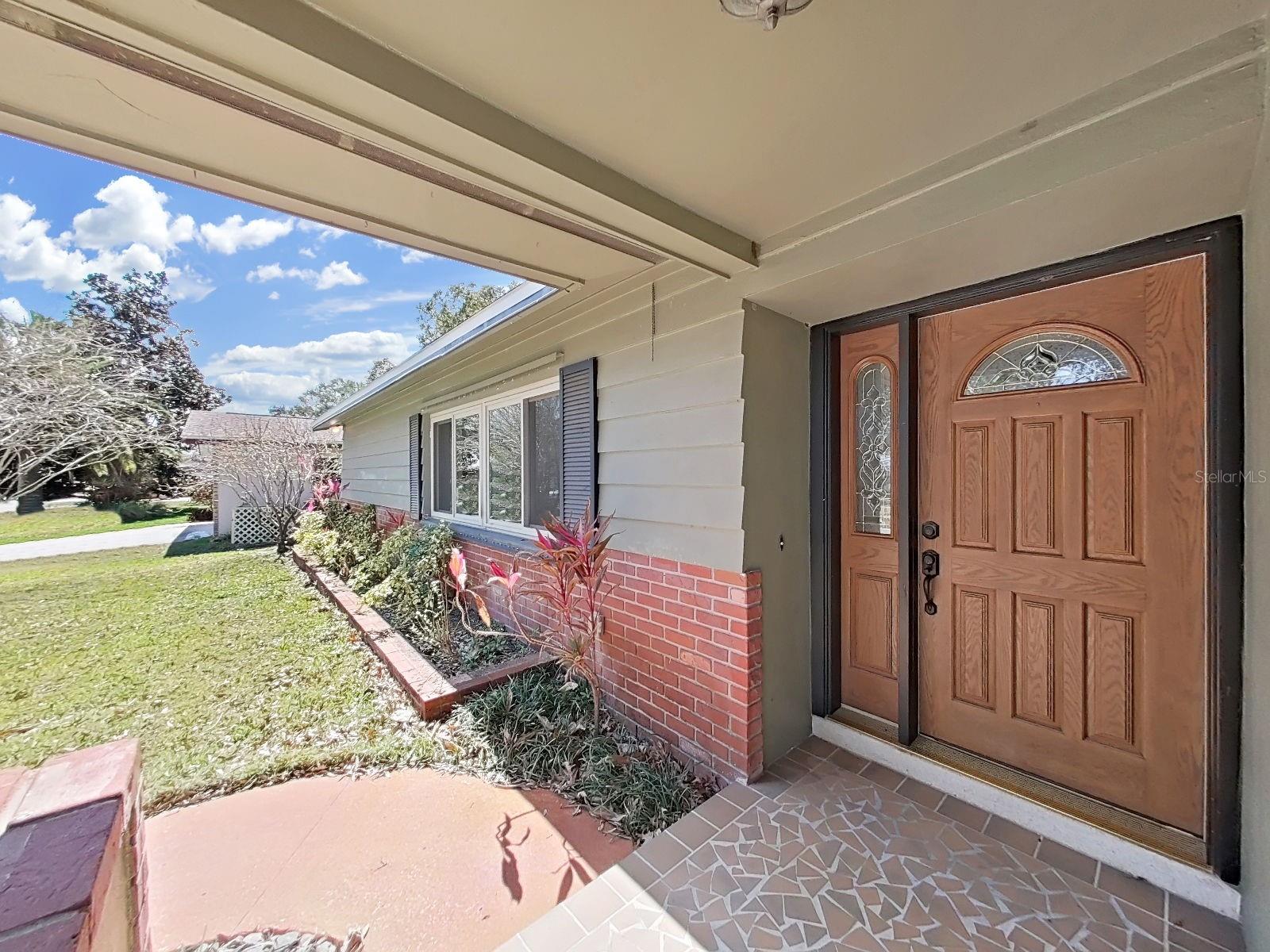 Covered front porch showcases mosaic tile entry and brick lined garden beds.