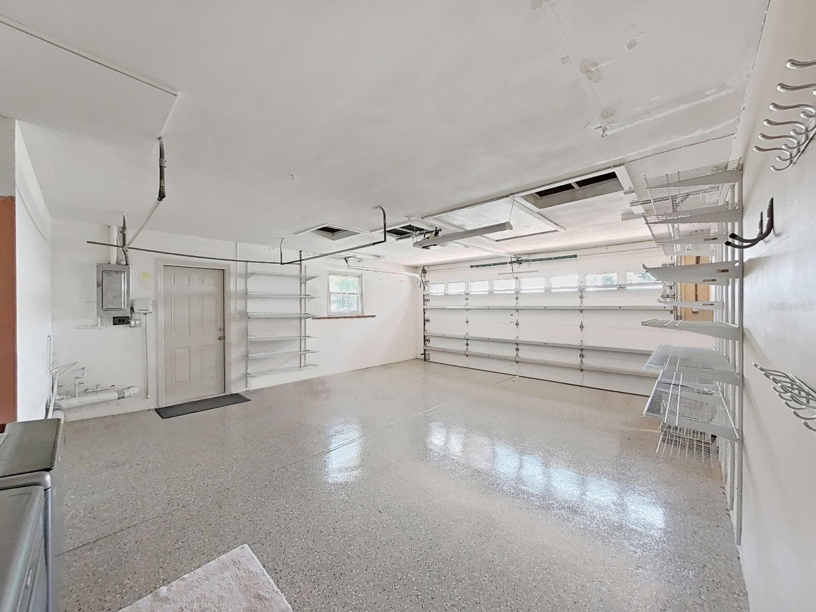 Oversized 2-Car Garage with hurricane-rated Garage Door (with NEW garage spring & pulley), gleaming finished floor, built-in shelving, offering exceptional storage and workspace potential. NEW Pedestrian side door & NEW Garage Door opener.