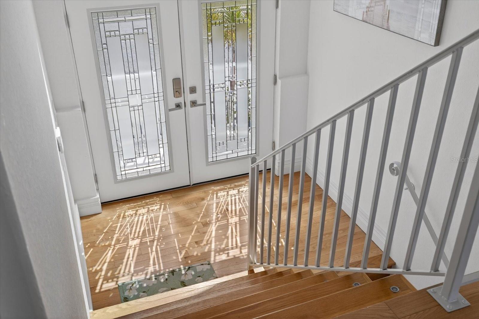 View looking down from Great Room to landing at front door with elegant lighting.