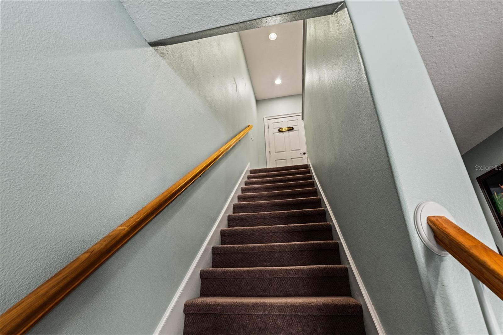 Carpeted staircase with wood railing and art-lined walls leading to the upper level of the home.