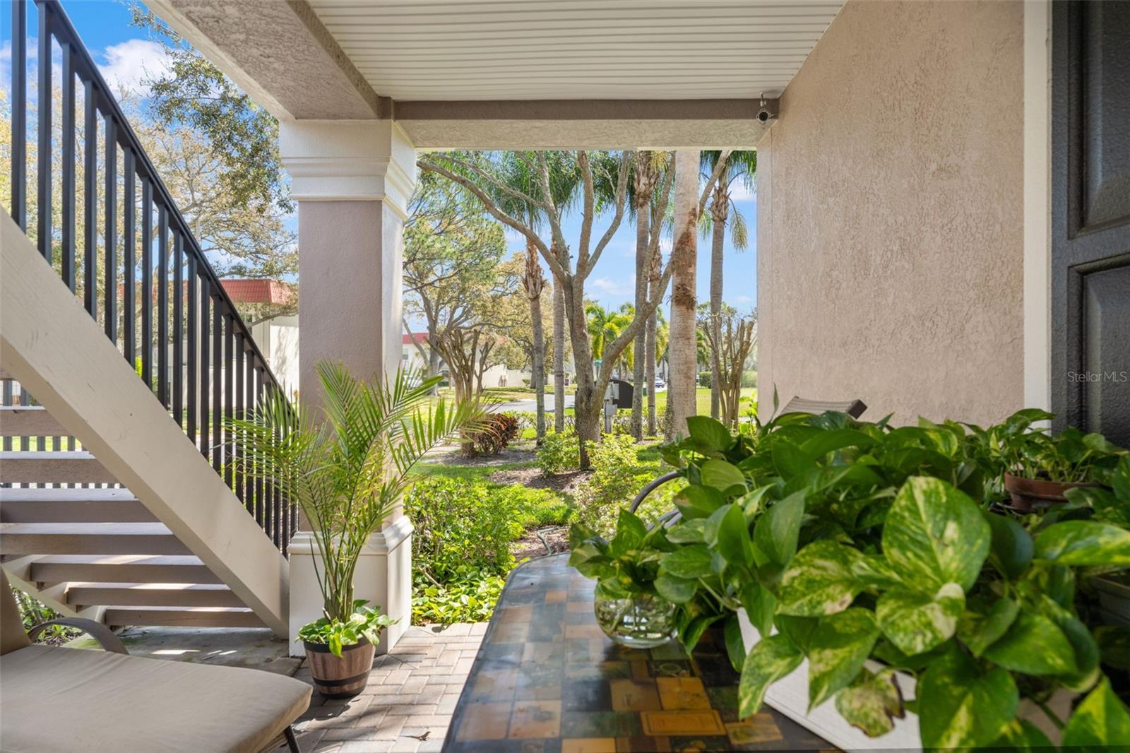 Covered outdoor seating area overlooking lush greenery and mature trees, creating a peaceful and welcoming entry.