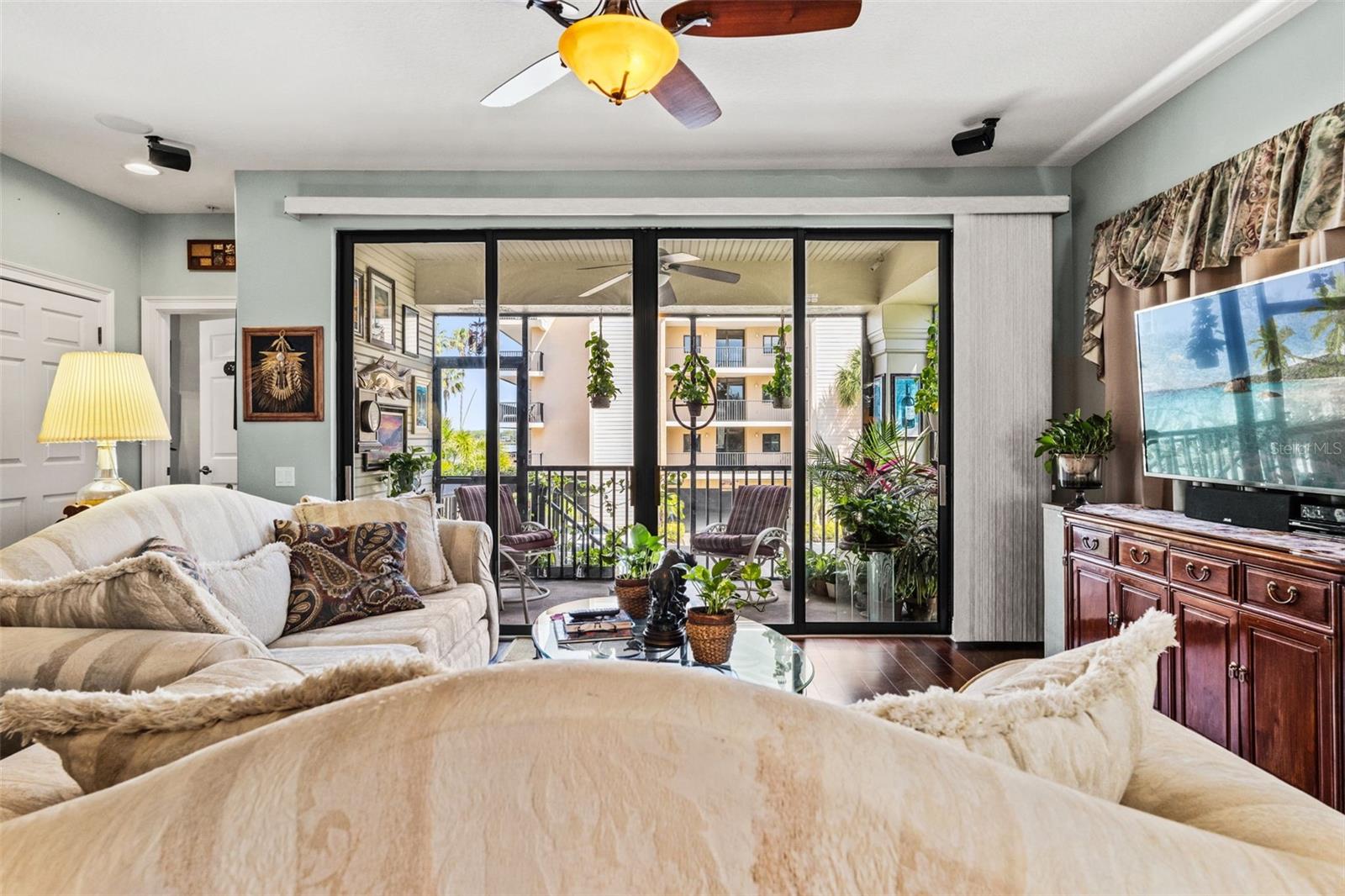 Spacious living room with rich wood flooring and large sliding glass doors that open to a covered balcony, filling the space with natural light.