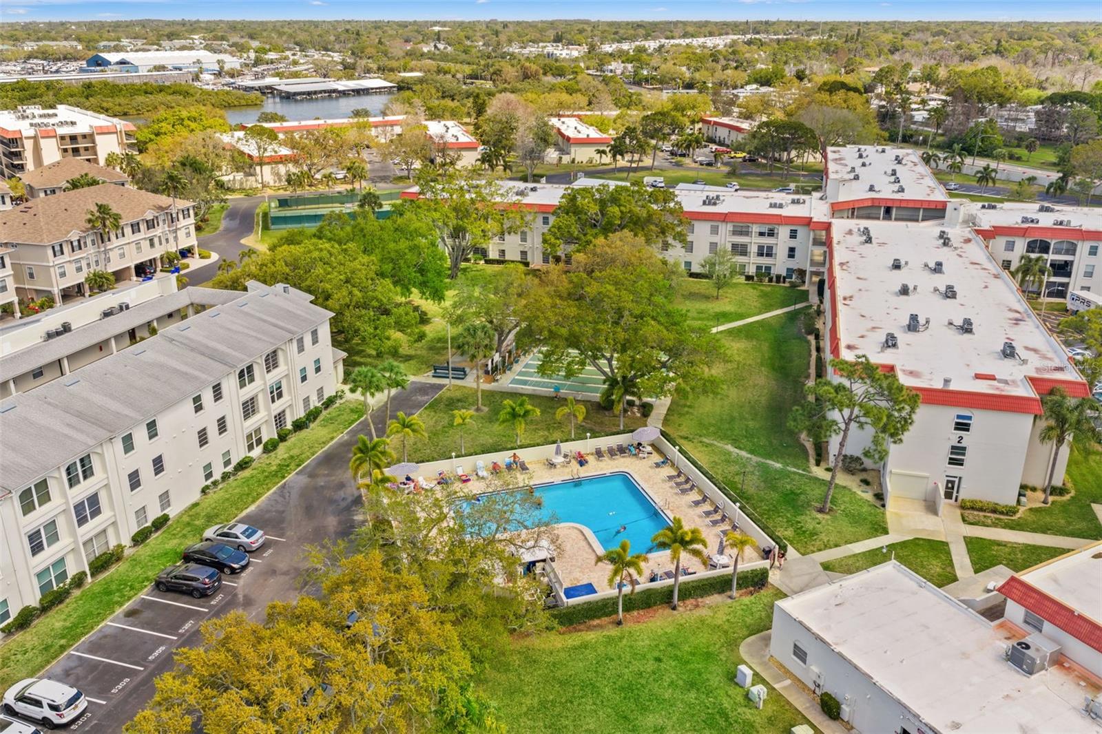 Elevated aerial view of the community grounds including pool, green spaces, and nearby residential buildings.