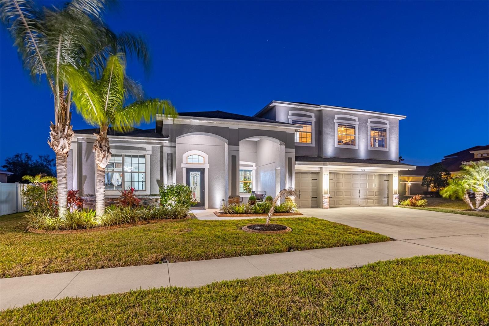 Dramatic twilight shot of the front elevation and palm trees with accent lighting.