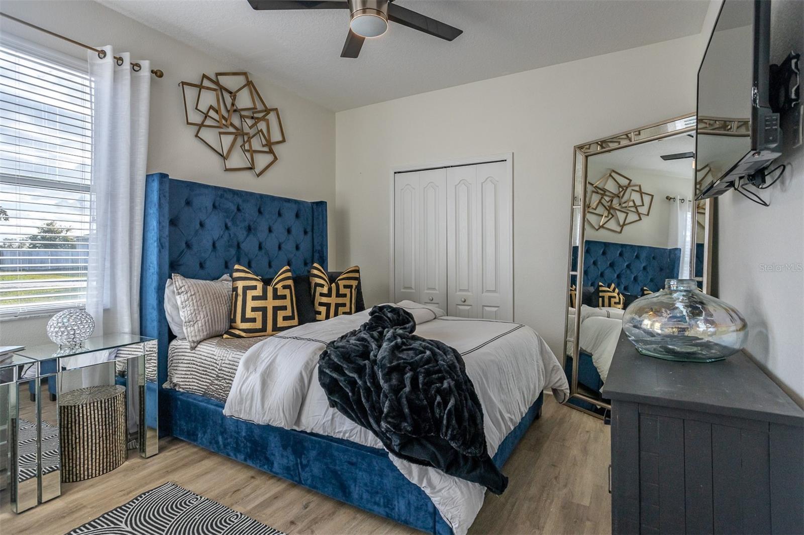 Primary suite featuring a blue velvet tufted headboard and luxury flooring.