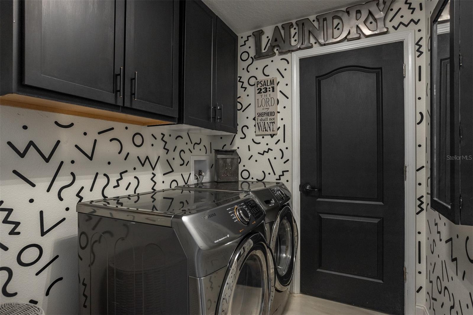 Laundry room featuring black custom cabinetry, high-end Samsung appliances, and designer wallpaper.