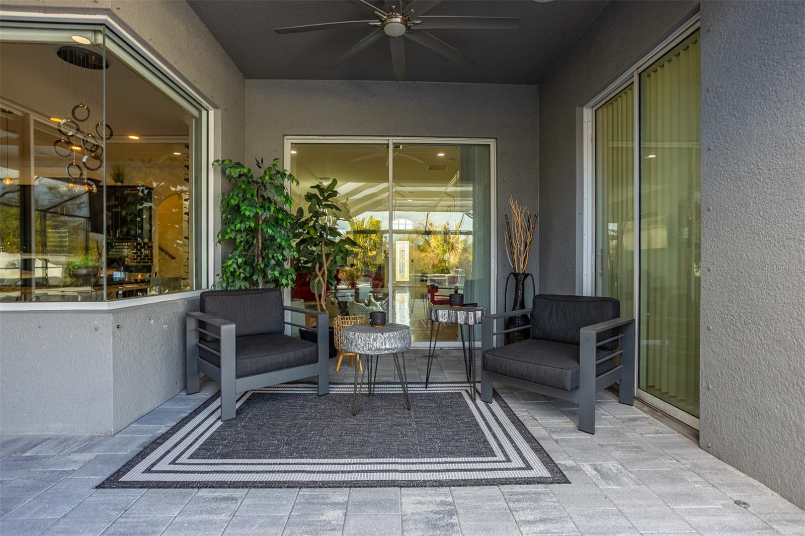 Modern covered patio with pavers, ceiling fan, and cozy outdoor seating area.