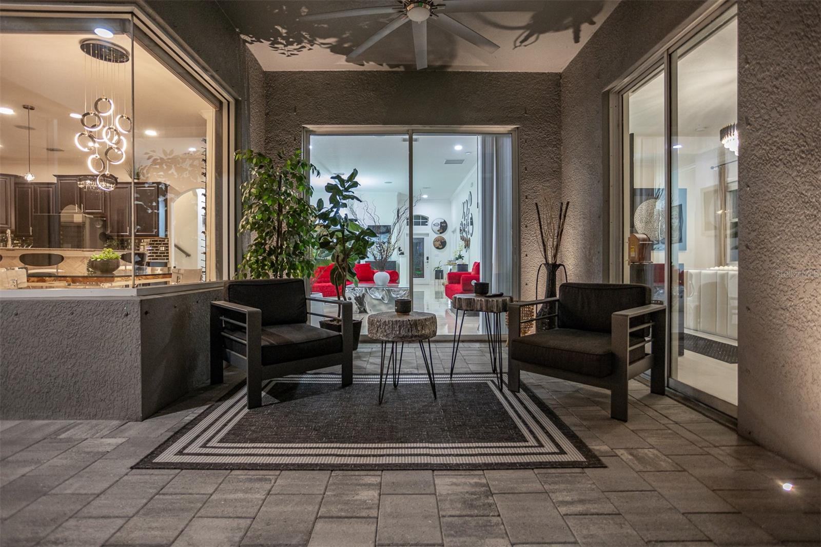 Shaded patio seating area illuminated at night, looking into the bright home interior.