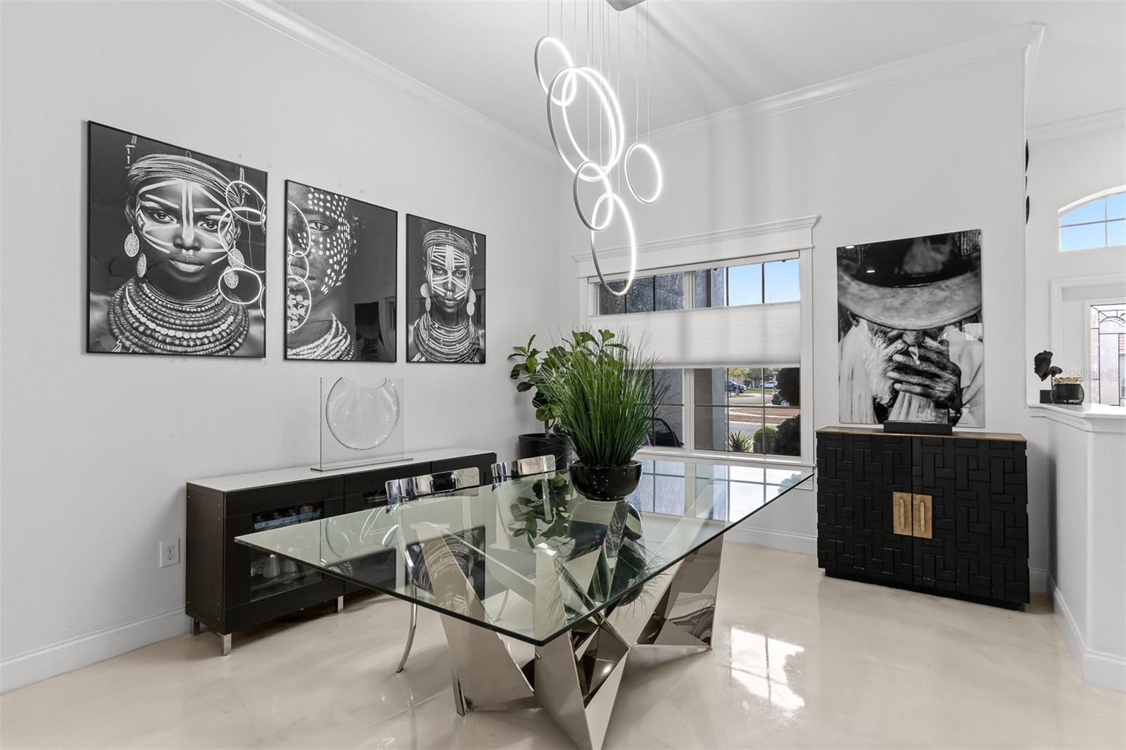 Formal dining area with a custom glass-top table, sculptural base, and ring-pendant lighting.