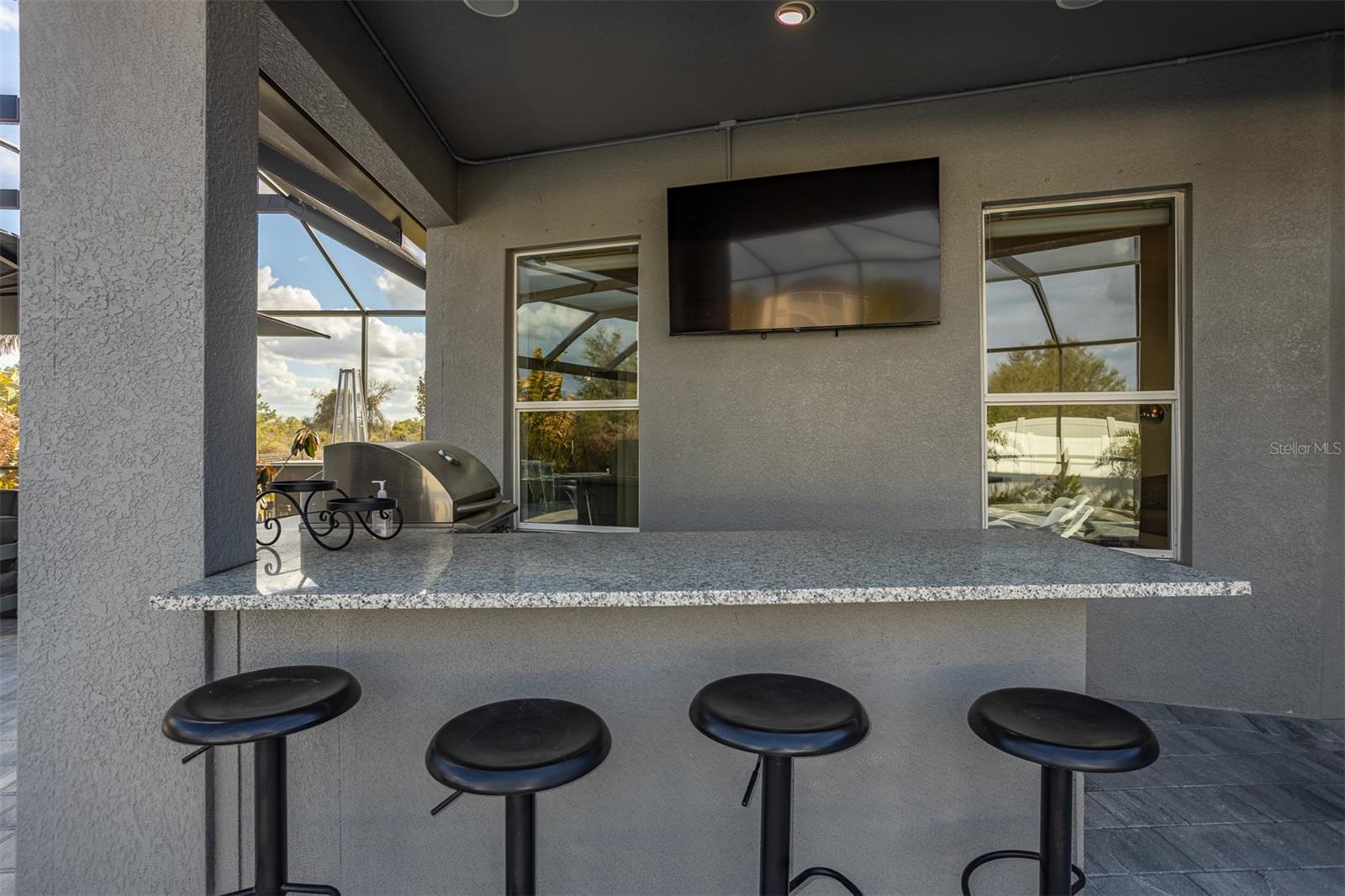 High-end outdoor kitchen with granite countertops, bar seating, and mounted TV.