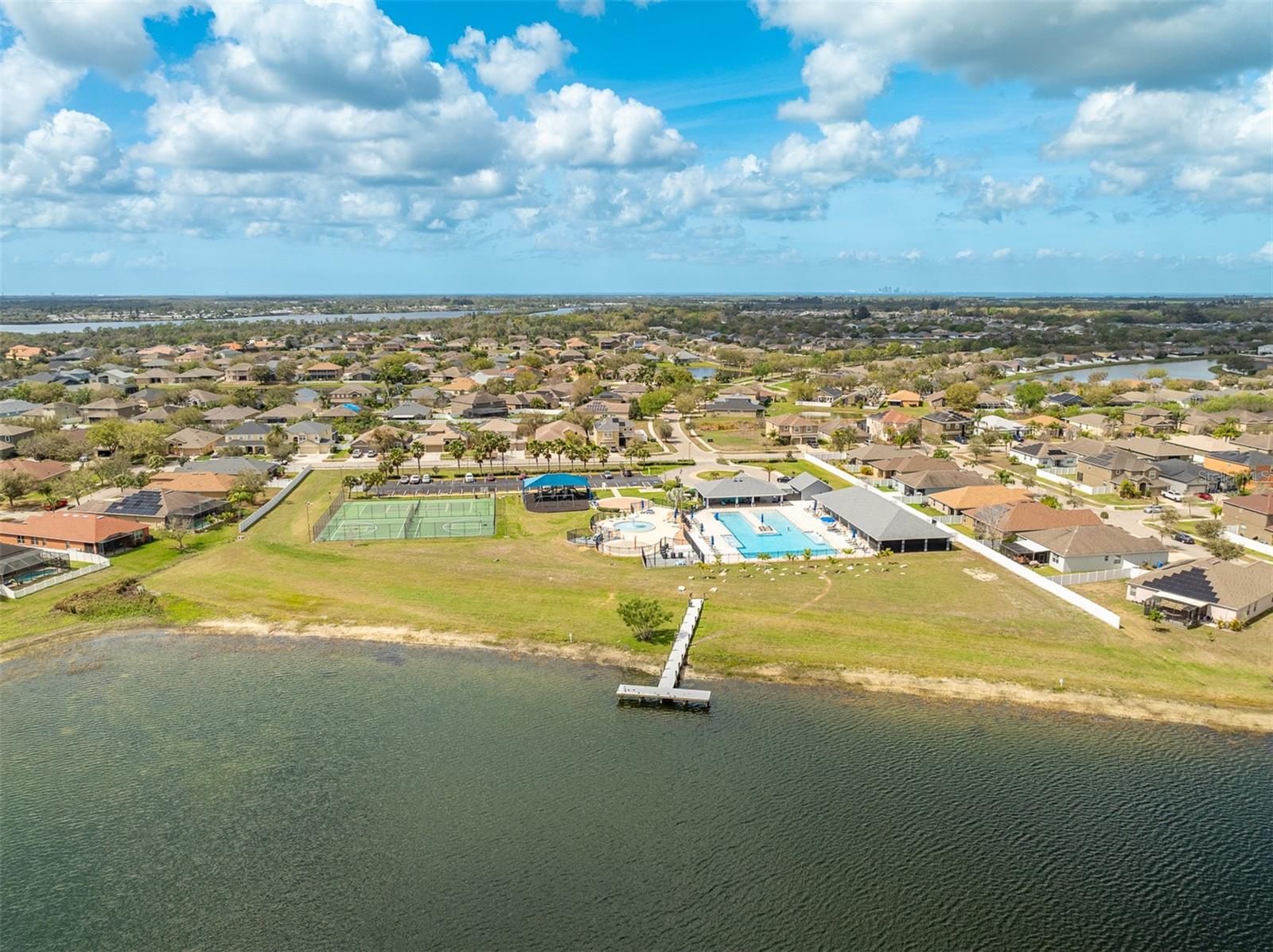Wide aerial shot of the community pool, sports courts, and private river dock.