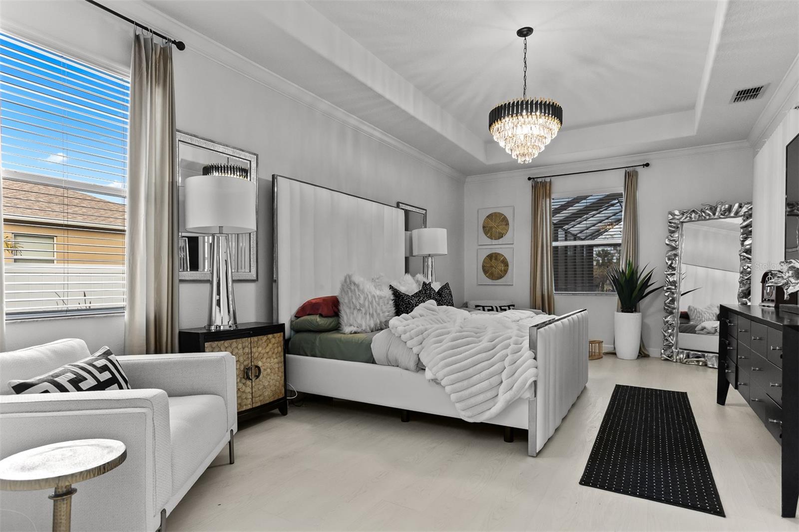 Grand primary bedroom with tray ceilings, elegant chandelier, and plenty of natural light.