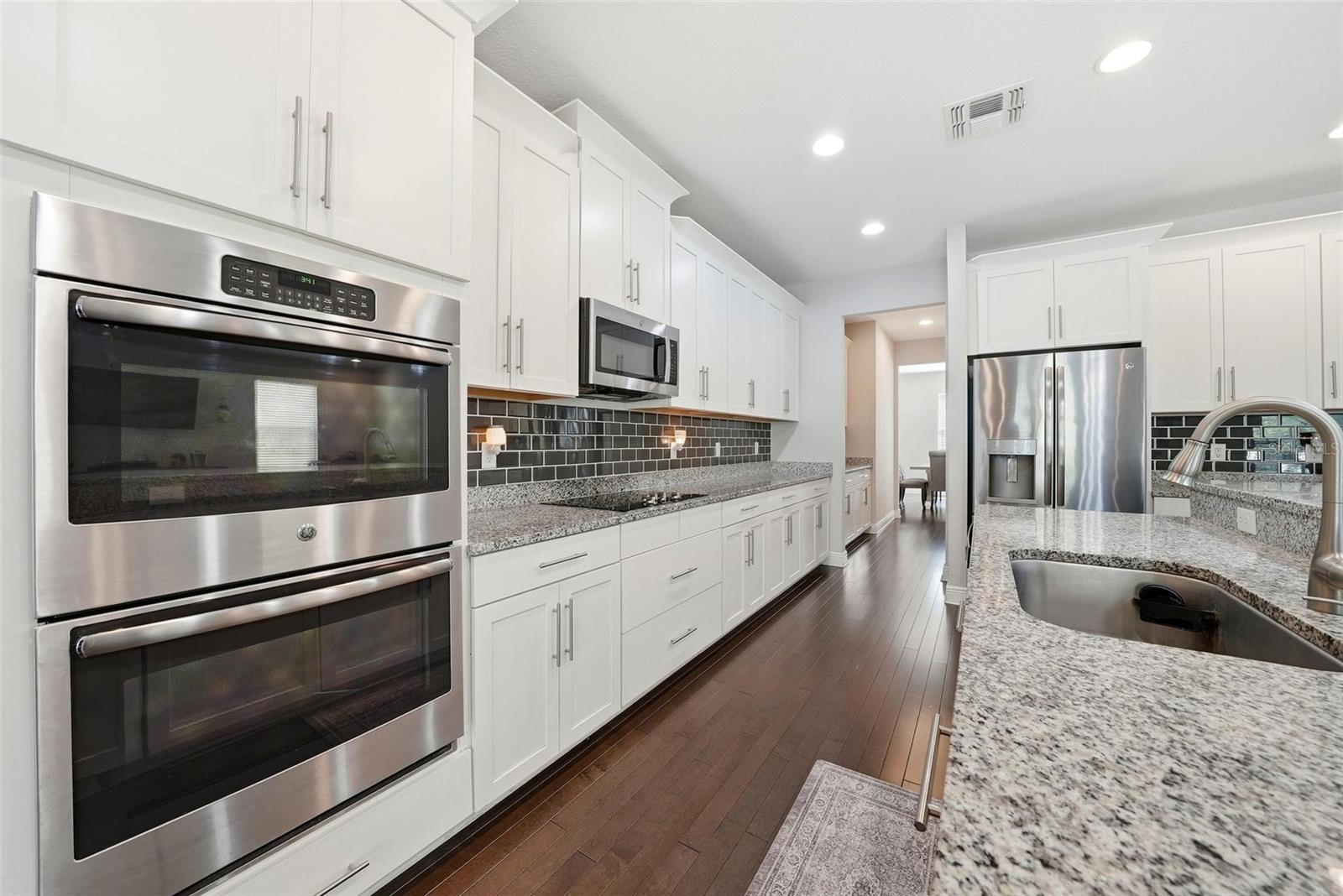 The kitchen is beautifully appointed with granite countertops, double ovens, and stainless steel appliances, all centered around an oversized island perfect for gathering and entertaining. A spacious pantry and abundant cabinetry provide exceptional storage, combining style and functionality in a truly impressive space.